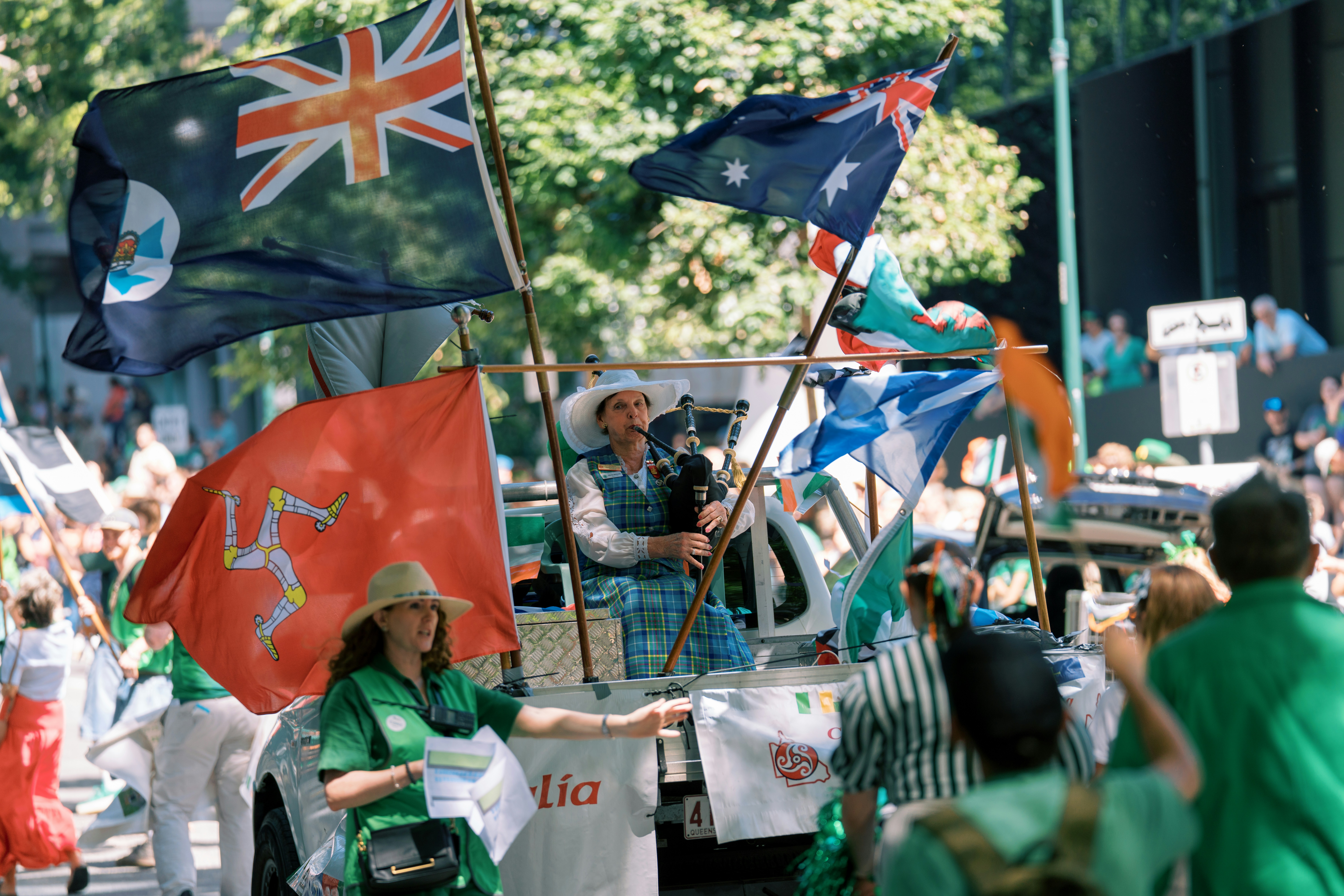 People waving flags during a parade with bagpiper.