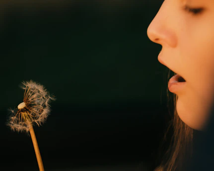 A young person blowing on a dandelion