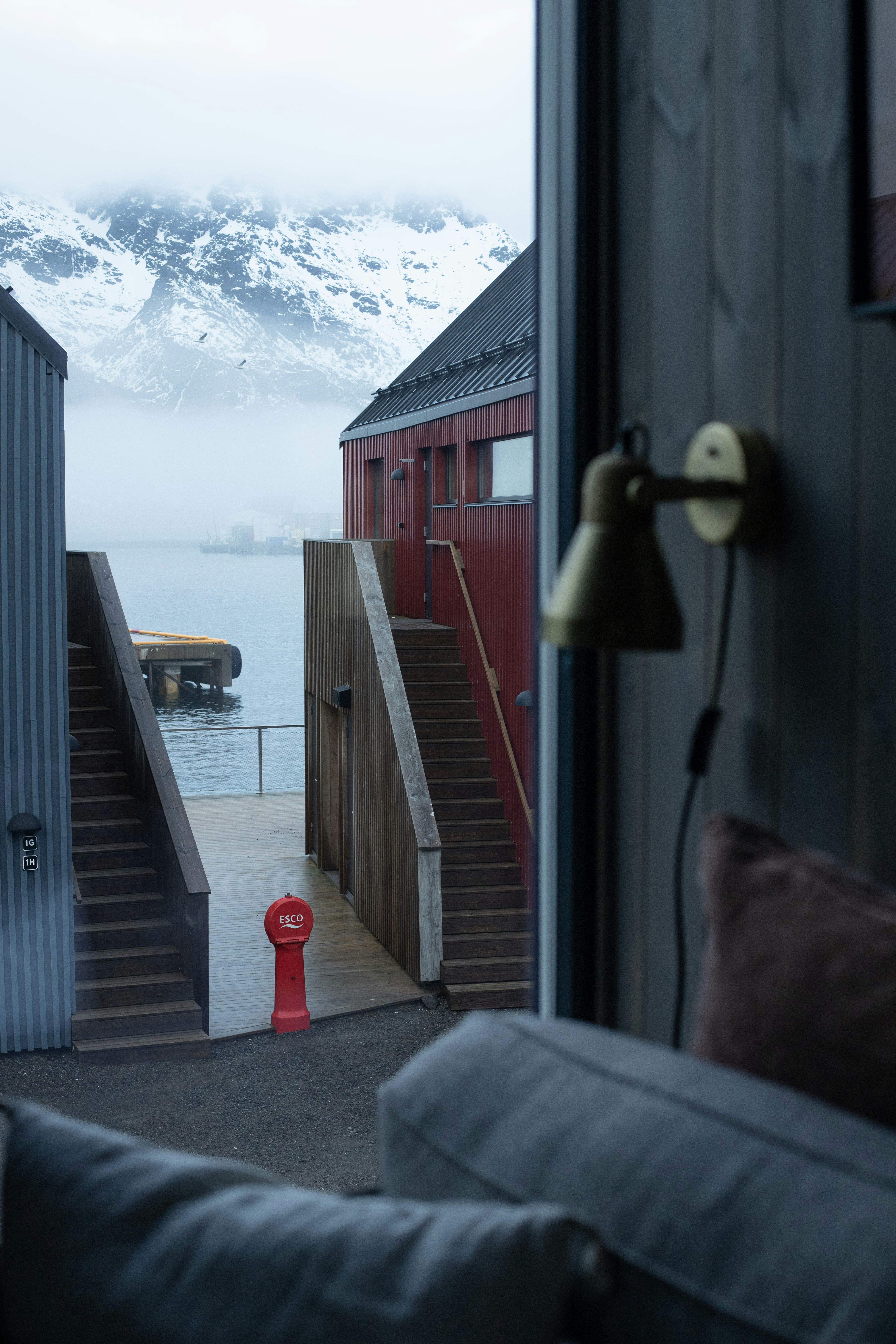 Edificio rojo con escaleras junto a una bahía con niebla y montañas