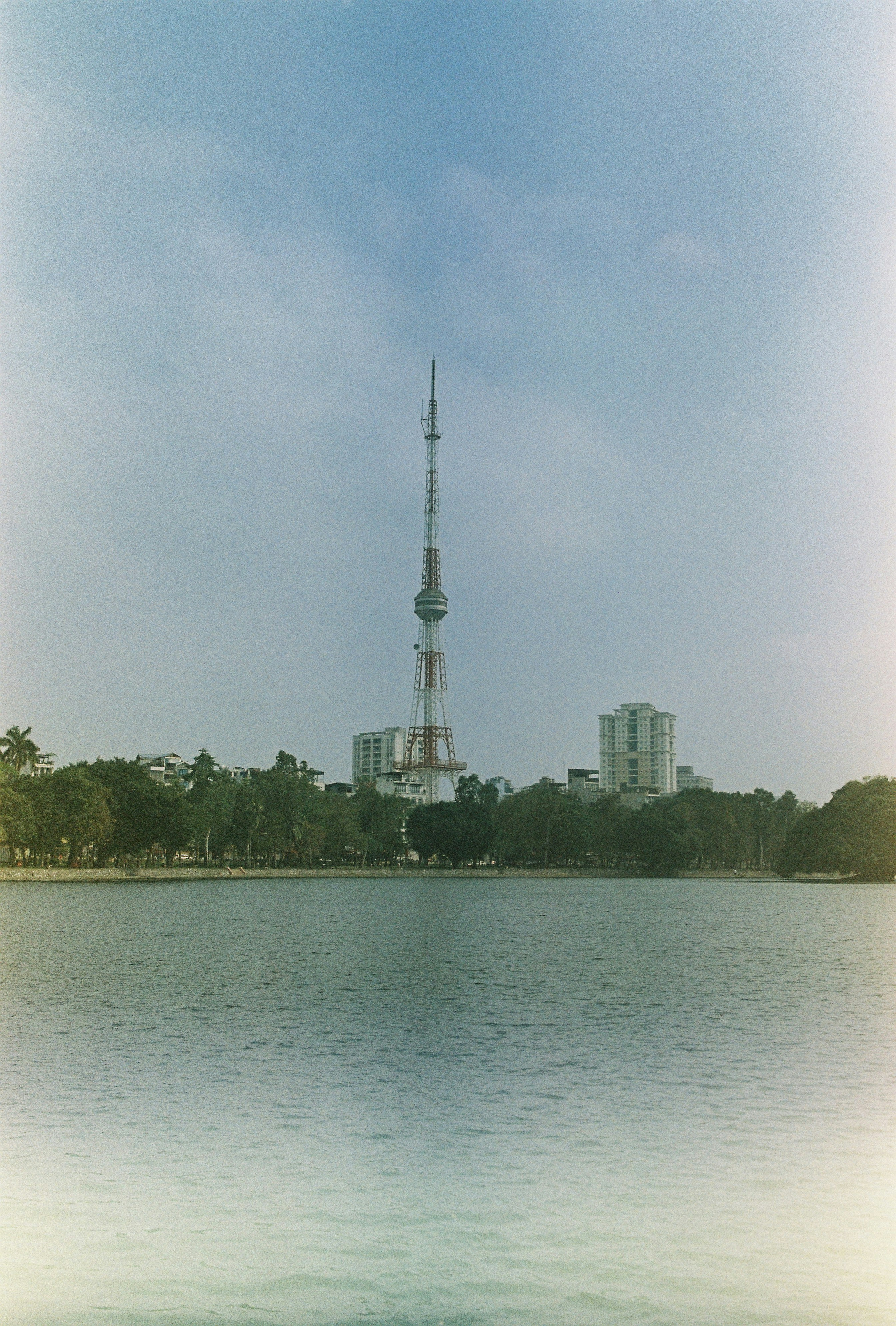 Tall tower stands over a calm lake and trees.