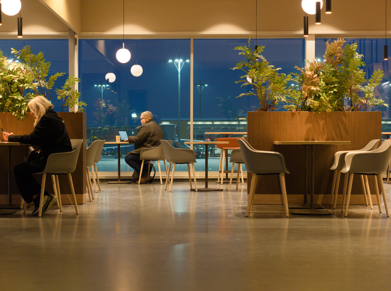 Business travellers working on laptops in a warmly lit airport cafe at dusk