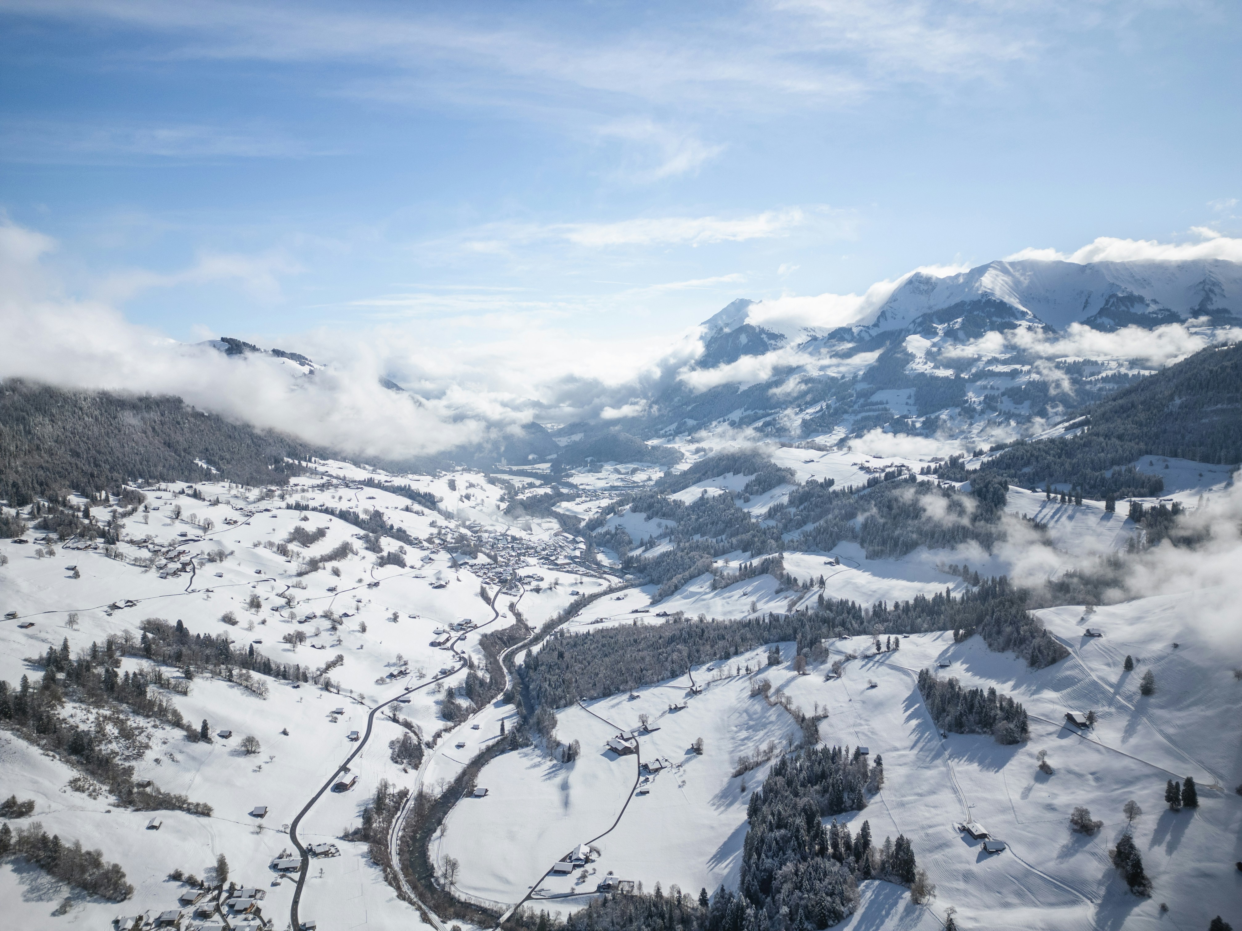 Snowy mountain valley with scattered houses and trees.