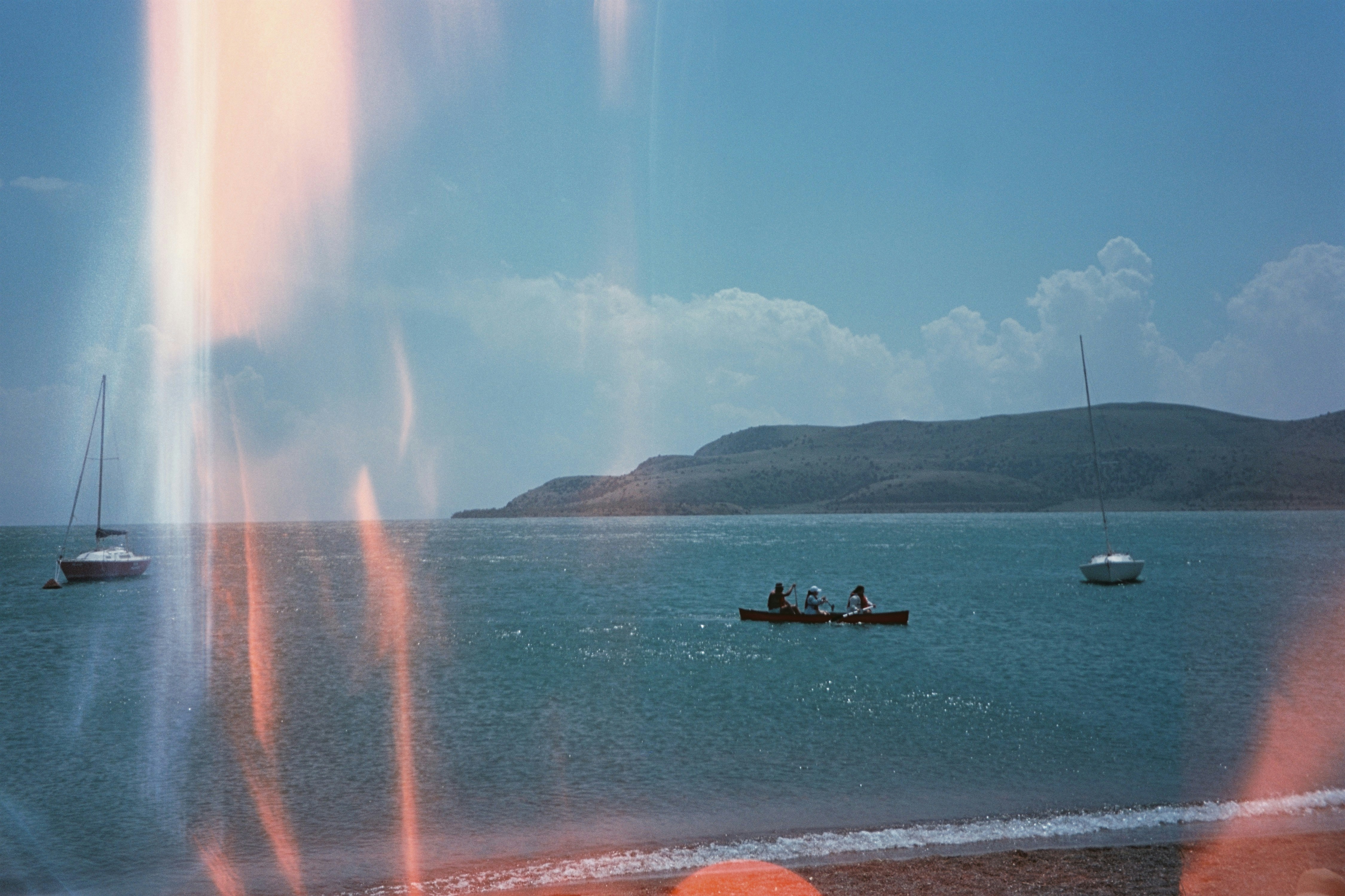 People on raft in ocean with sailboats and island