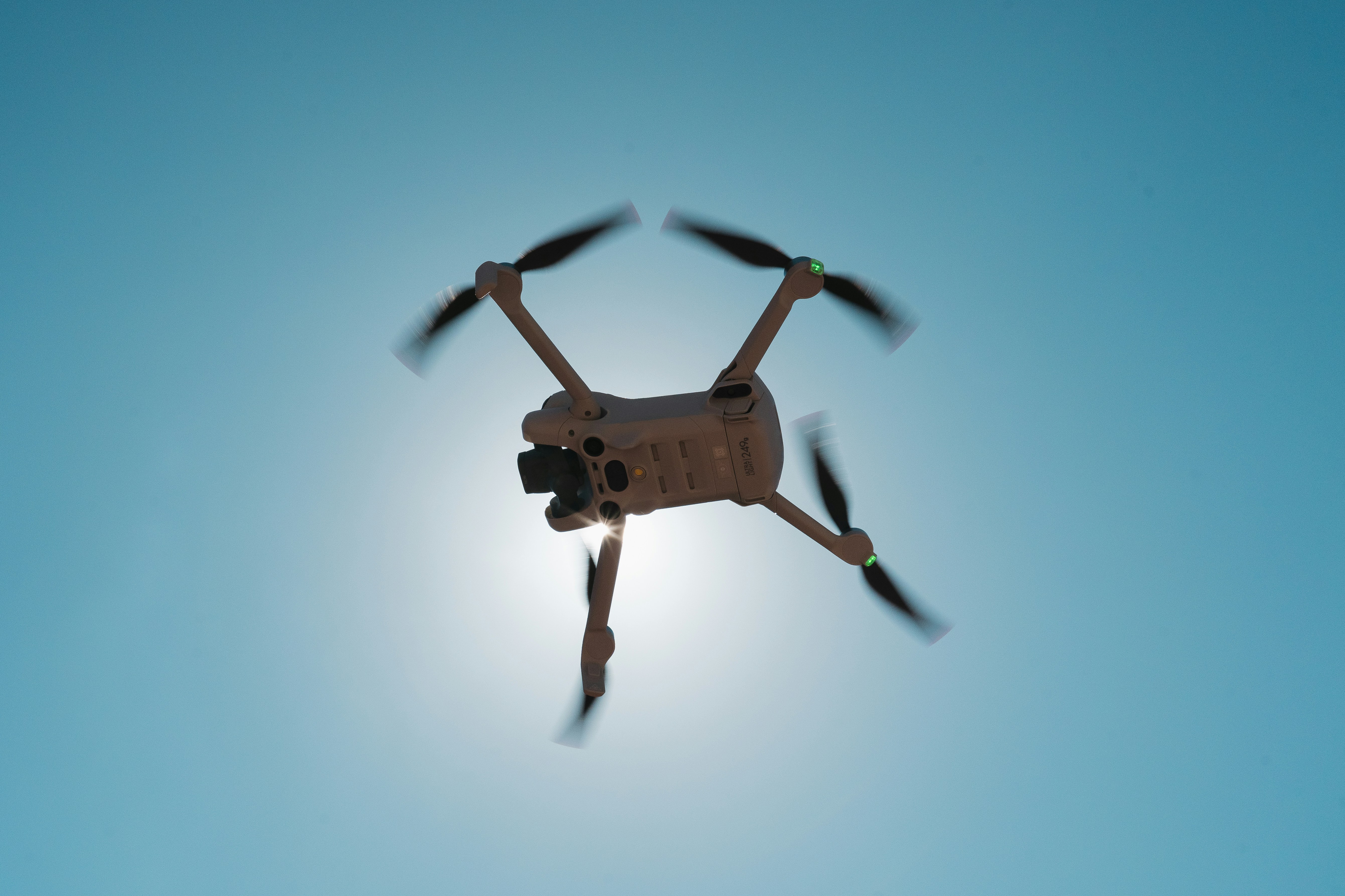 A drone flying against a bright blue sky.