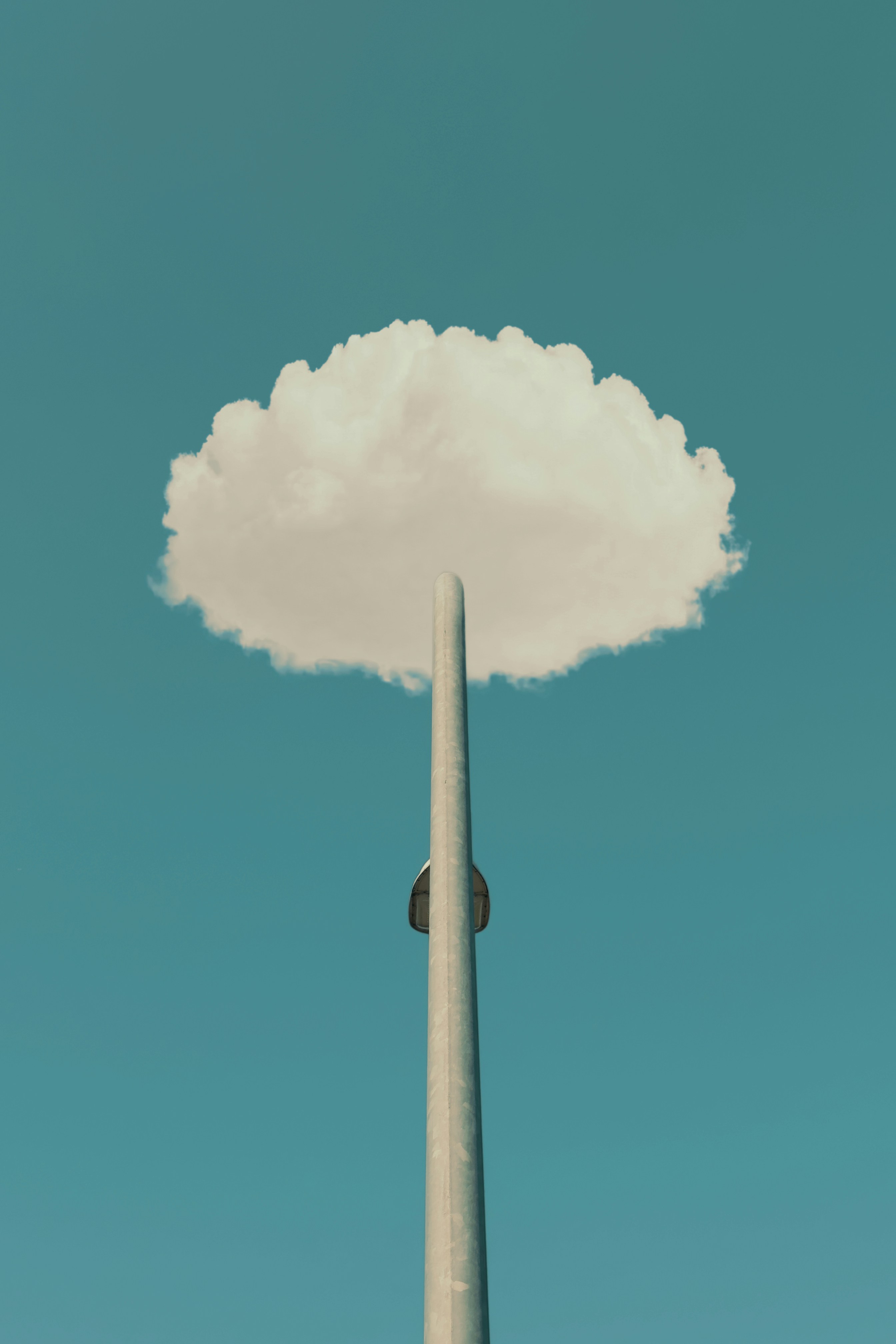 A cloud rests atop a pole against a blue sky.