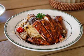 Sliced grilled chicken breast over pasta with vegetables.