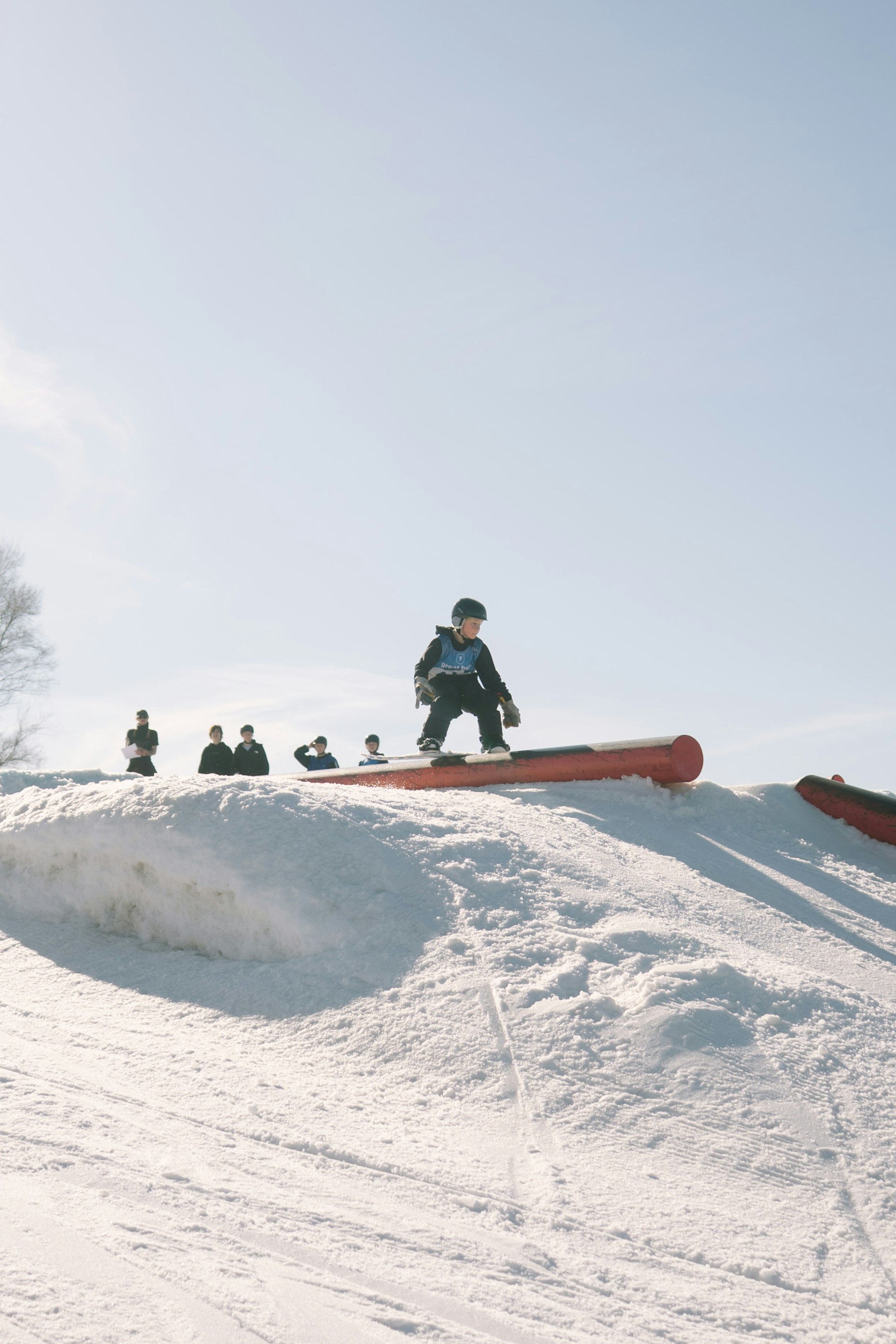 Young snowboarder learning on a beginner park feature with friends watching