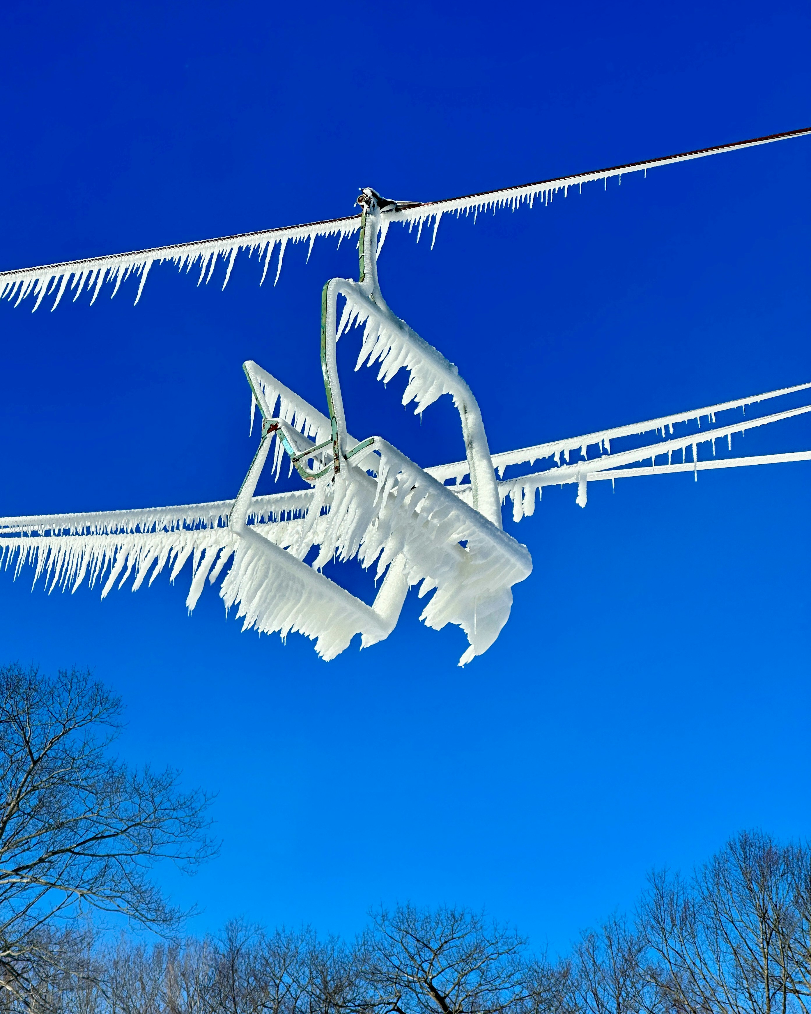 Ski lift covered in ice against a bright blue sky.