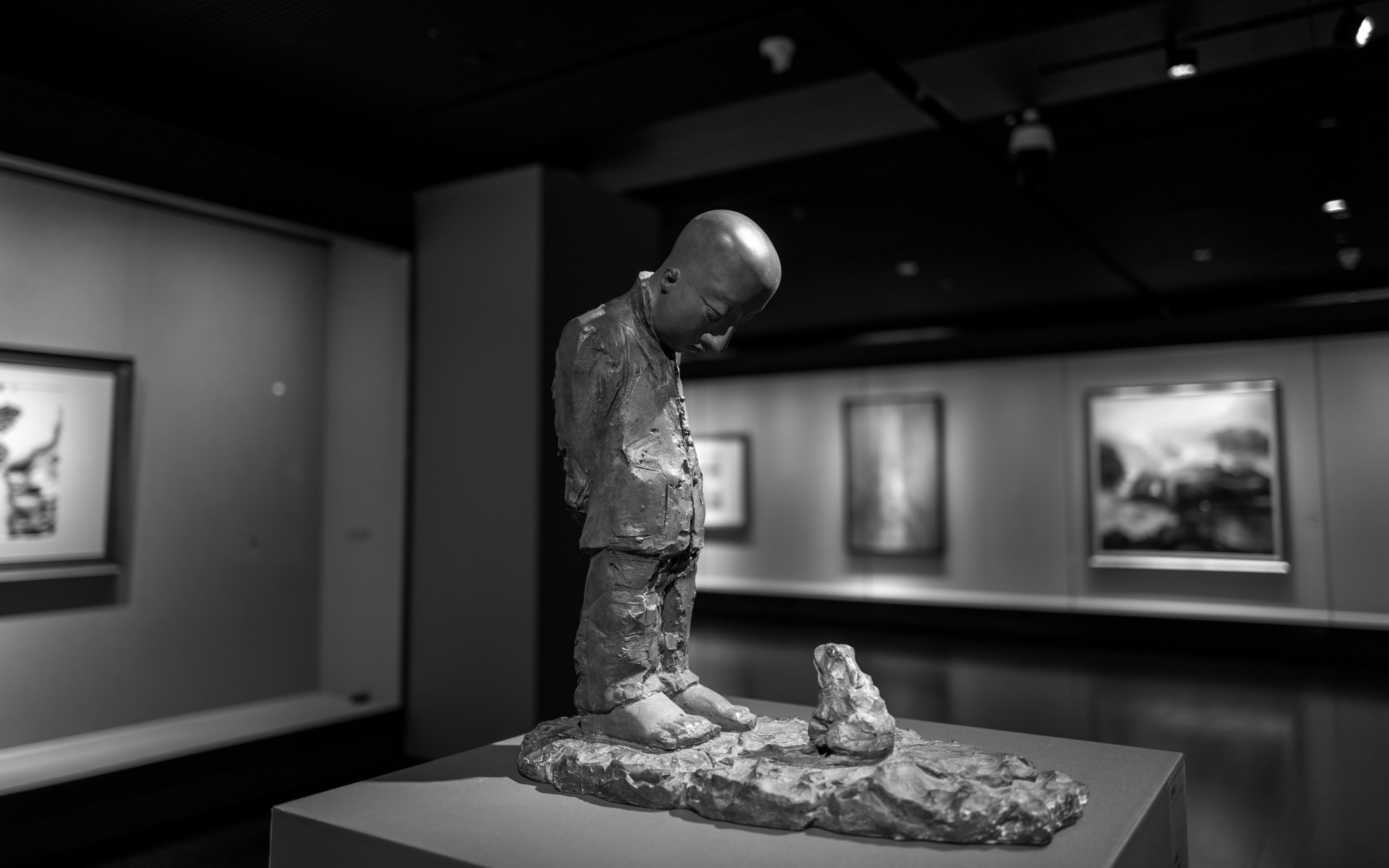 Sculpture d’un garçon regardant un petit objet.