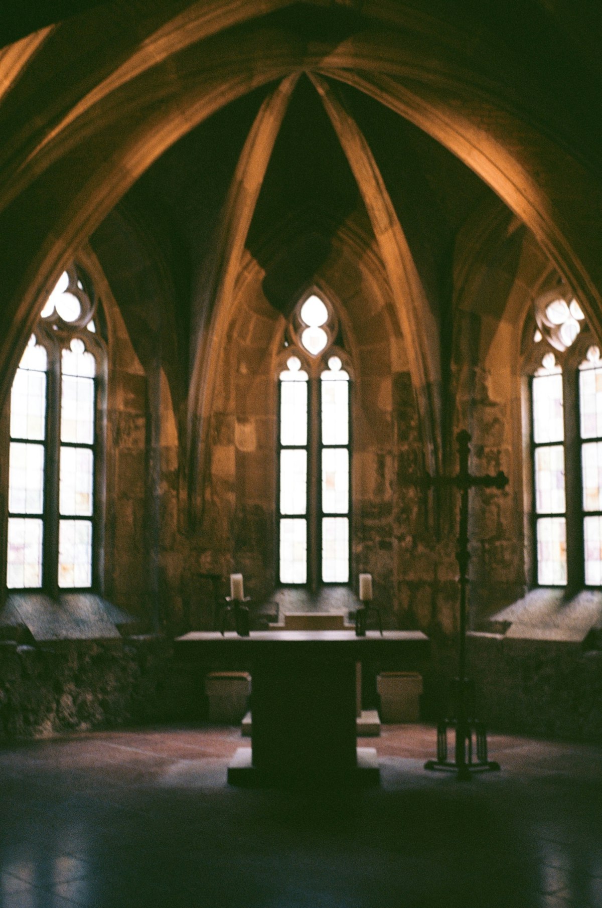Stone chapel interior with a cross at the altar, arched windows admitting quiet light