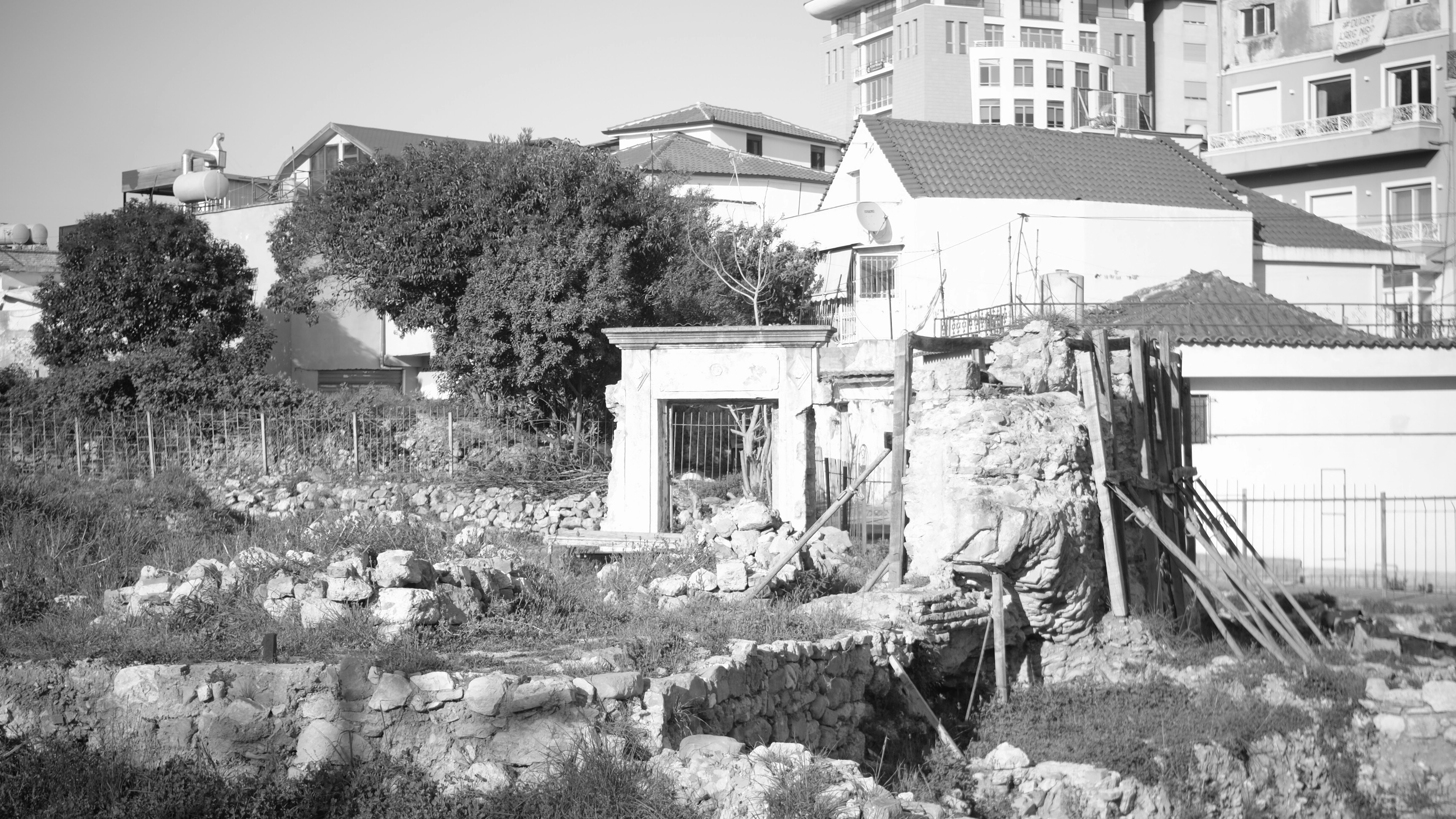 Rovine di una struttura antica con edifici moderni dietro.