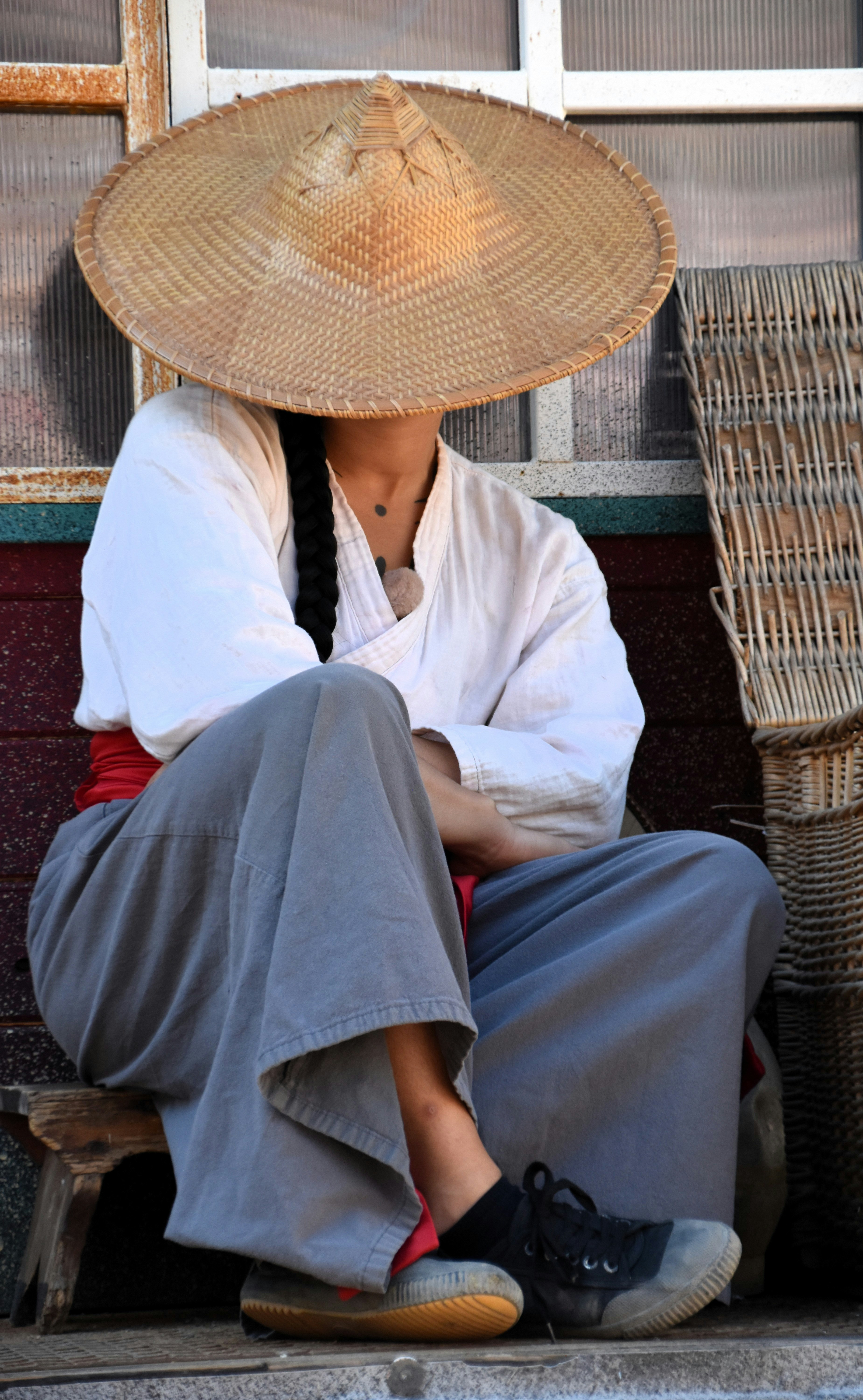 Person in conical hat sitting outdoors near woven baskets.