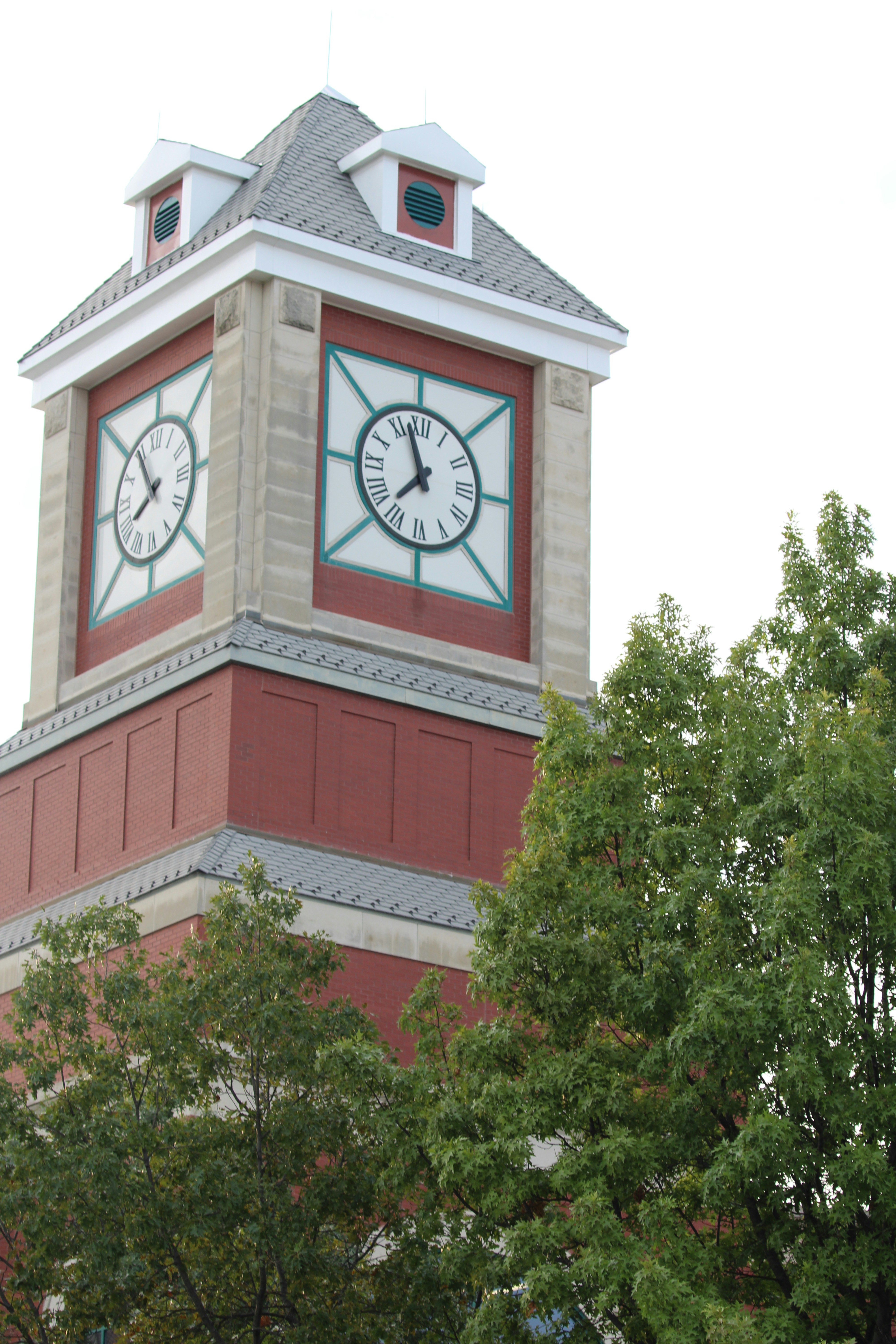 Uma torre de tijolos com dois relógios e árvores verdes.