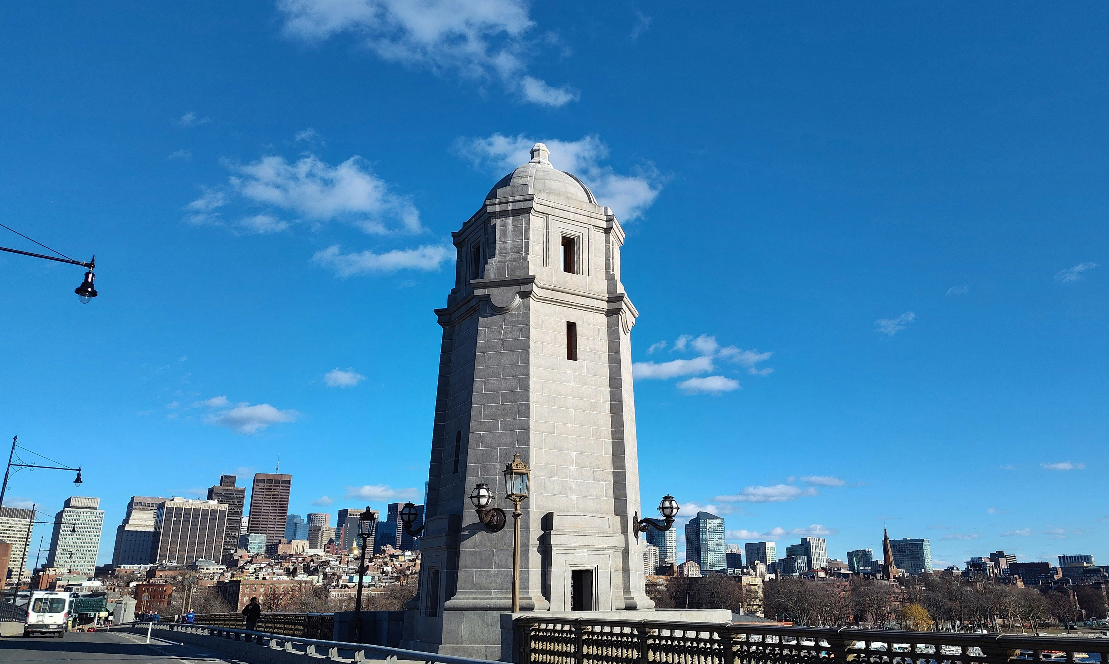 Stone tower on a bridge with city skyline.