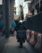 Person riding a scooter down a narrow city alley.