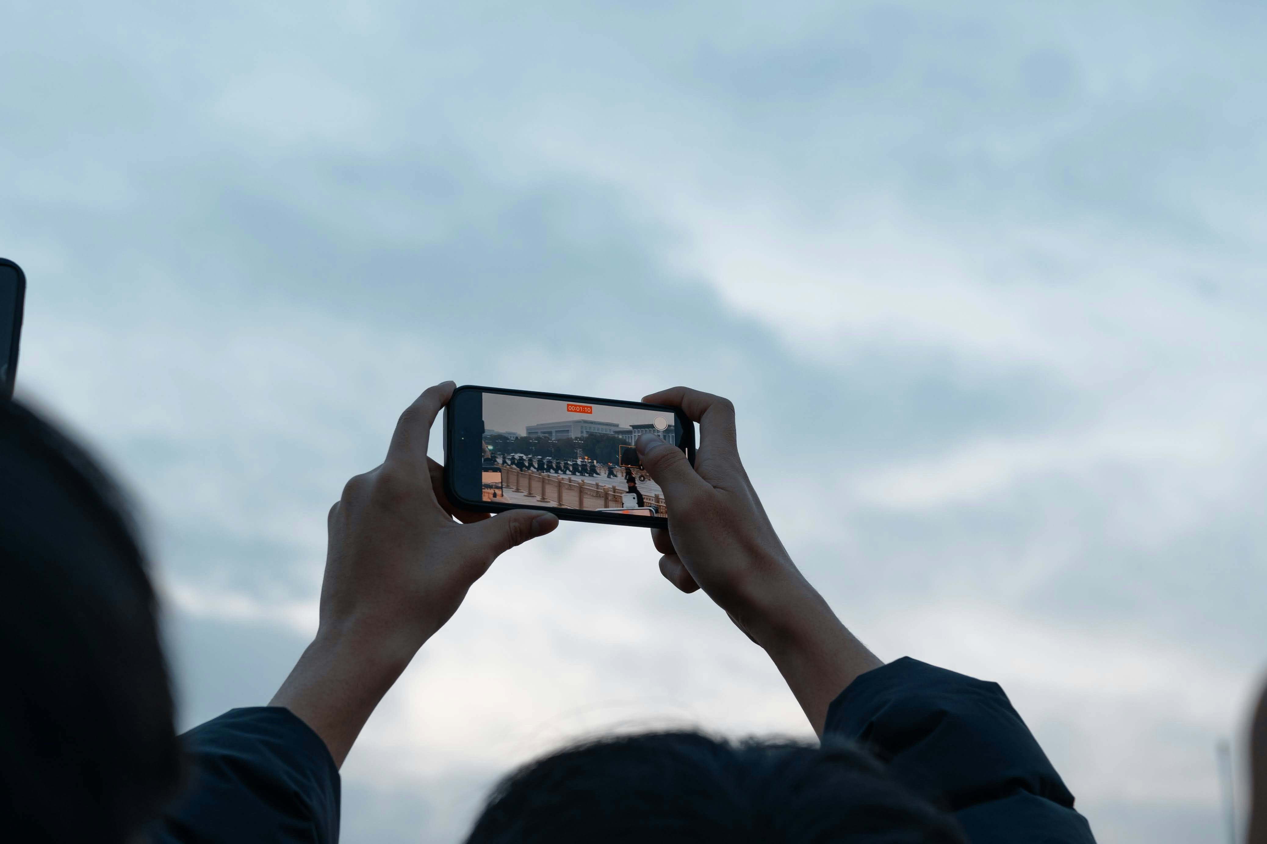 Hands holding a smartphone while recording a distant event