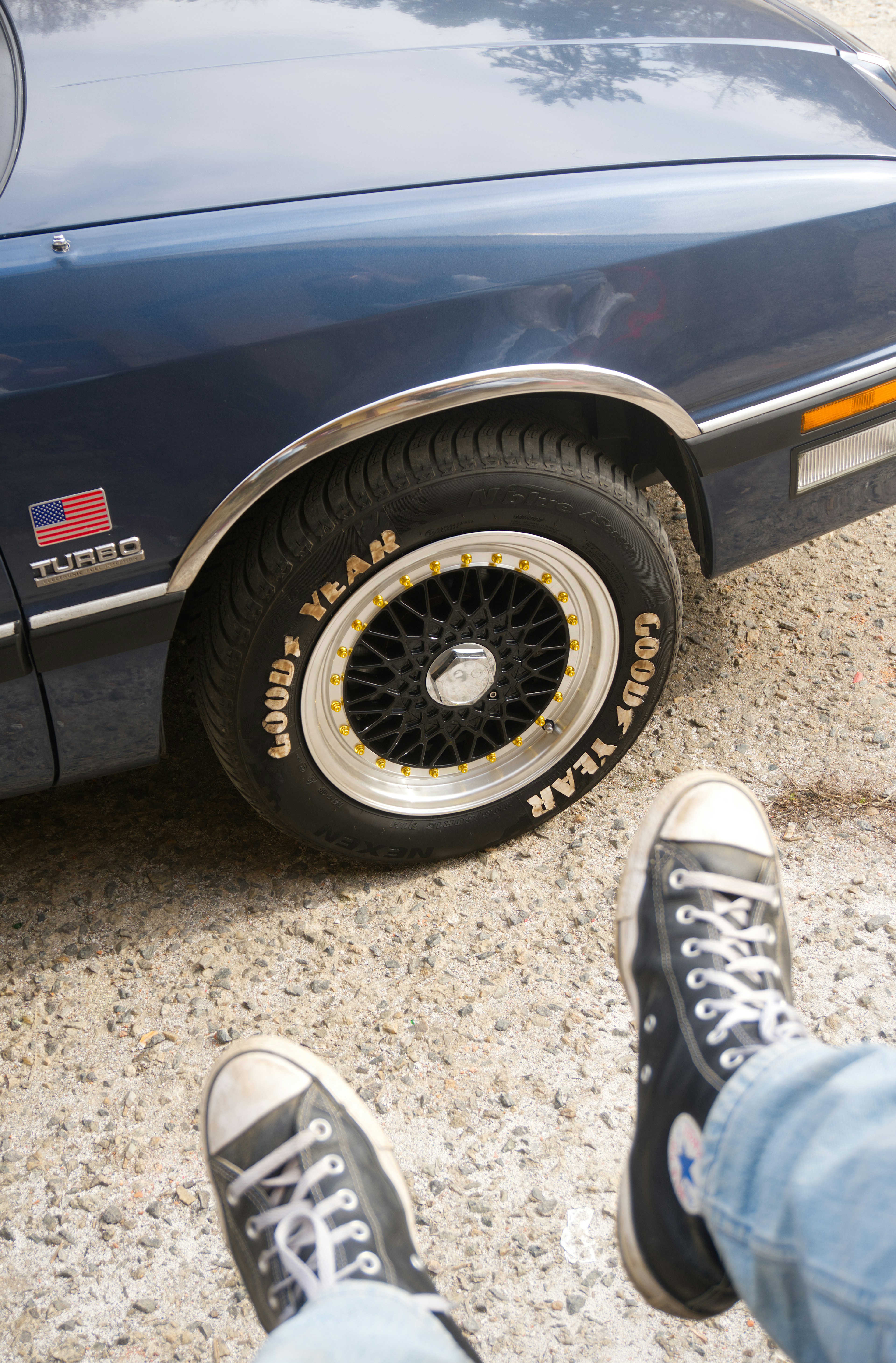 Primer plano de una rueda azul de coche y unas zapatillas