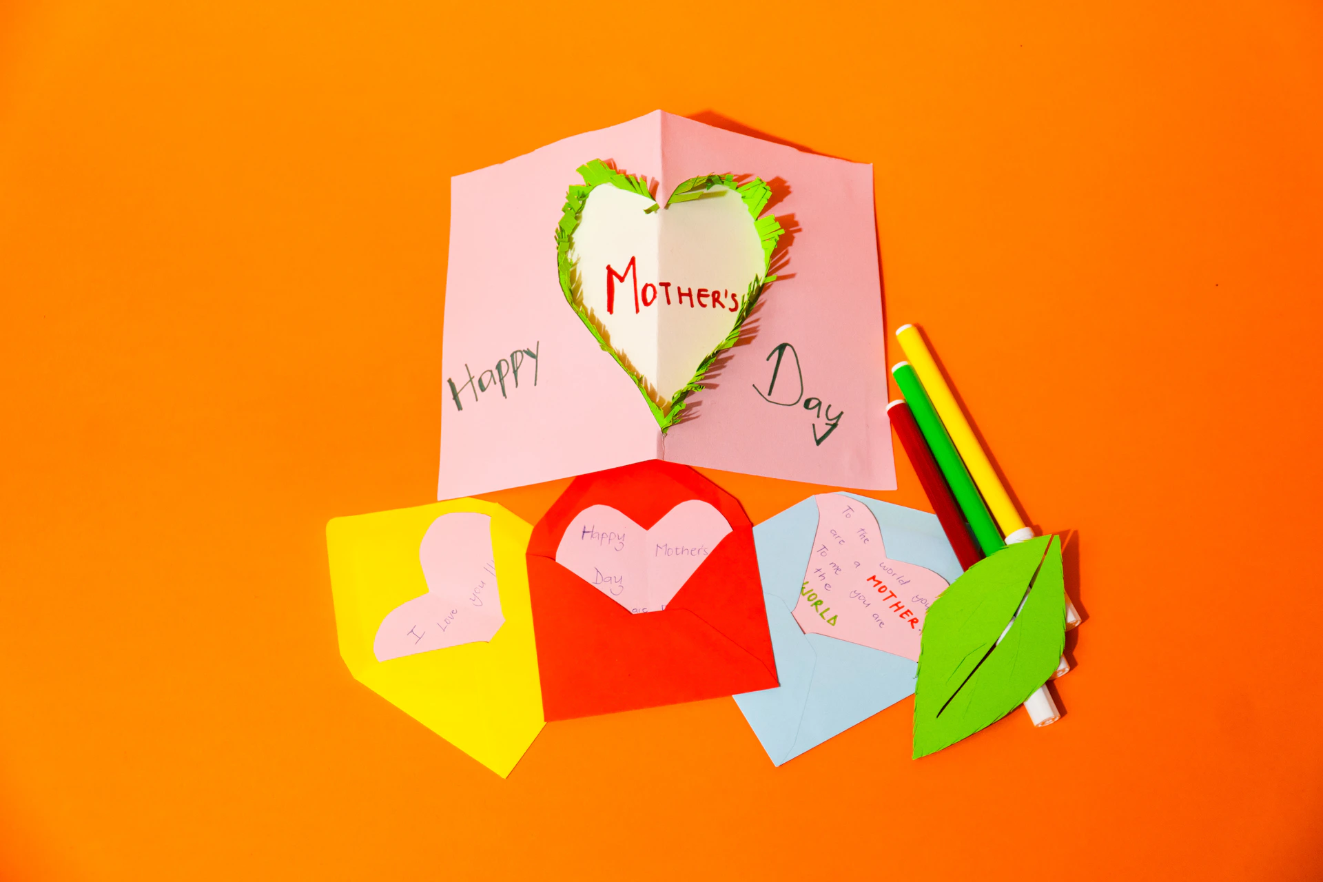 Handmade mother's day cards and art supplies on orange background