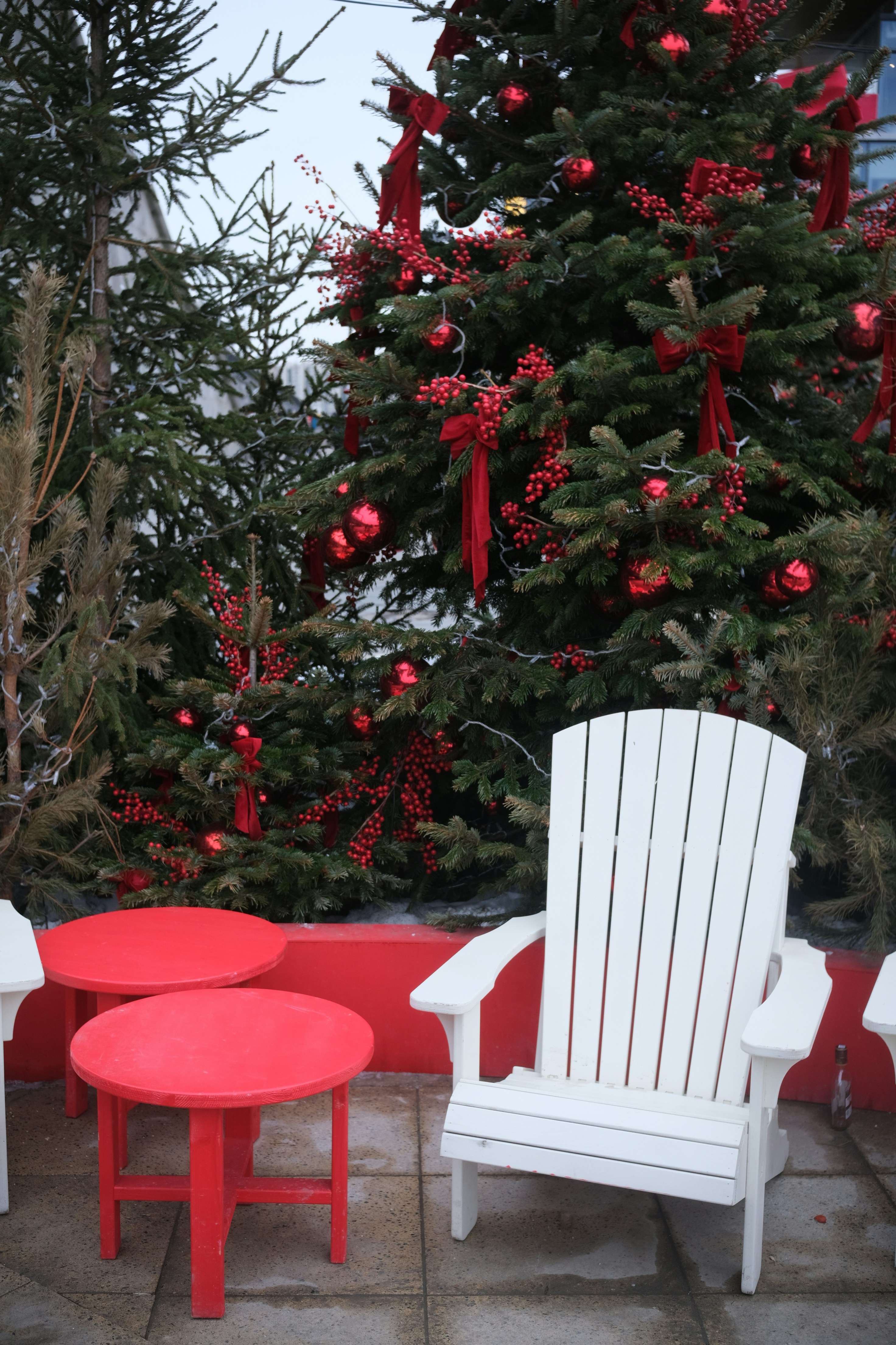 Decorated christmas tree with white chair and red tables.