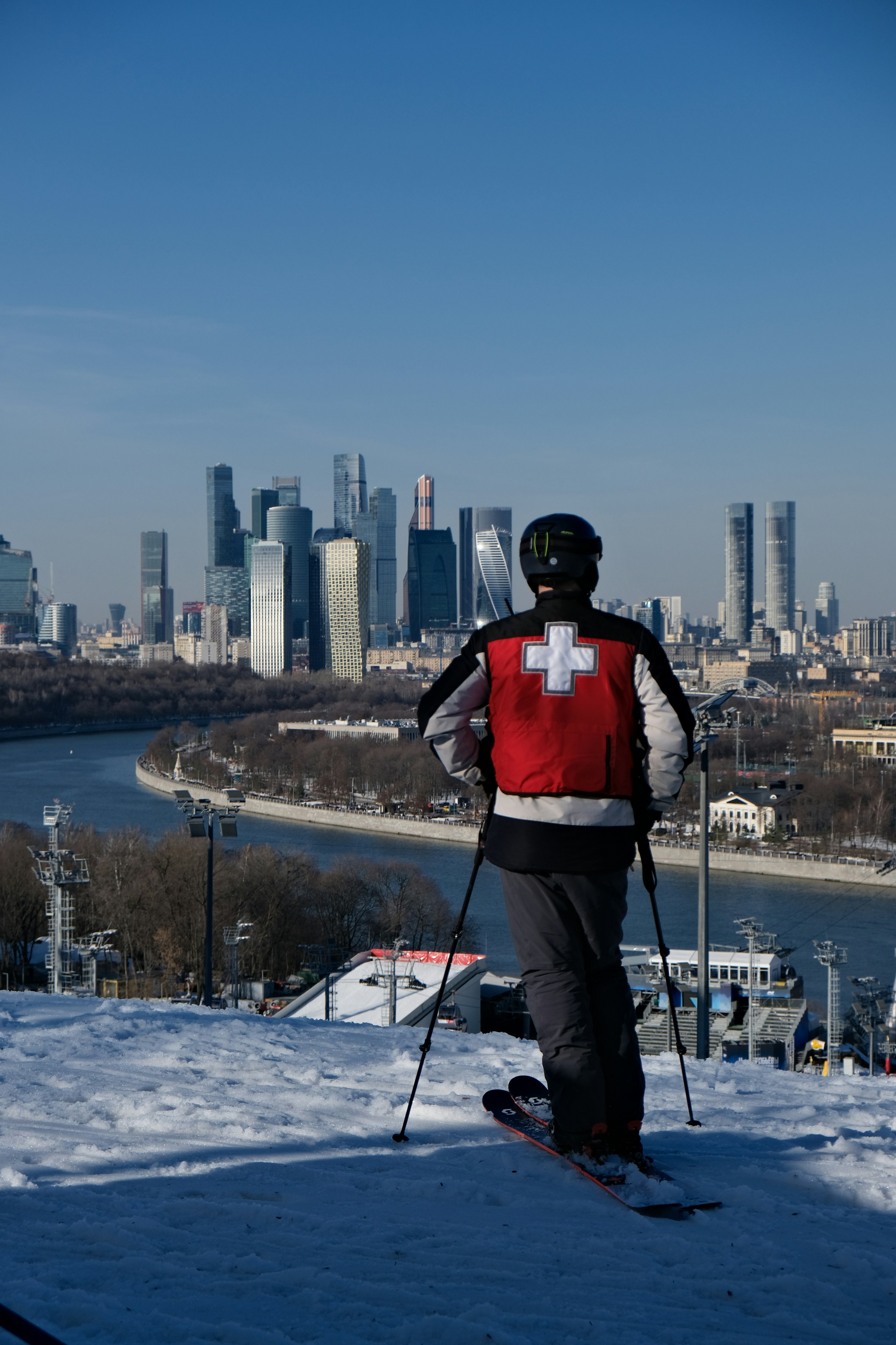 Skier in red vest overlooks city skyline from snowy hill
