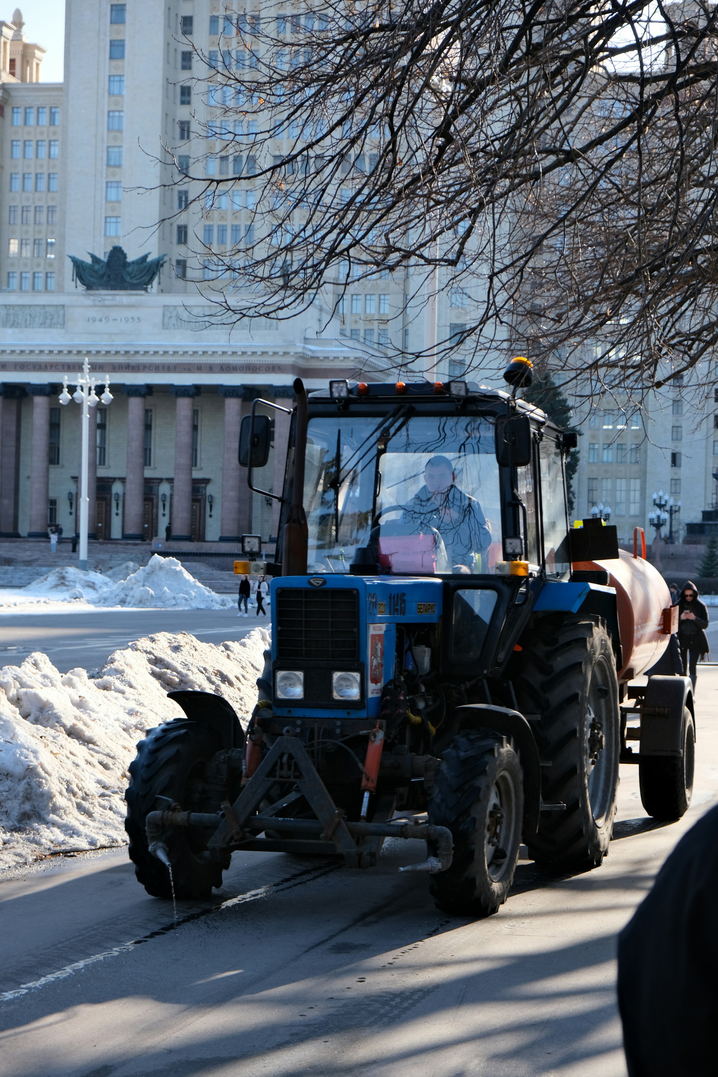 Blue tractor with attached water tank on a street.