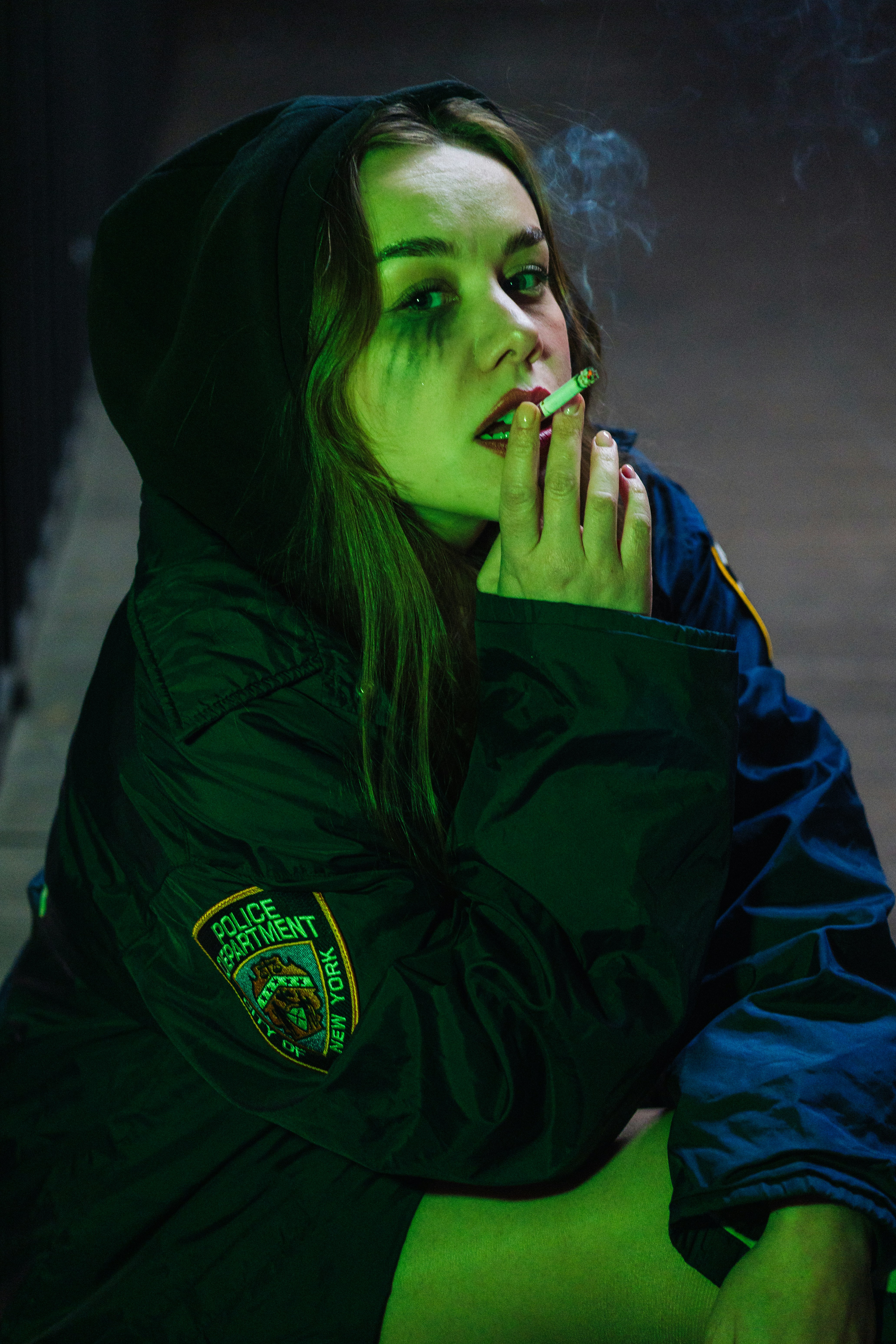 Woman in police jacket smoking cigarette with green lighting