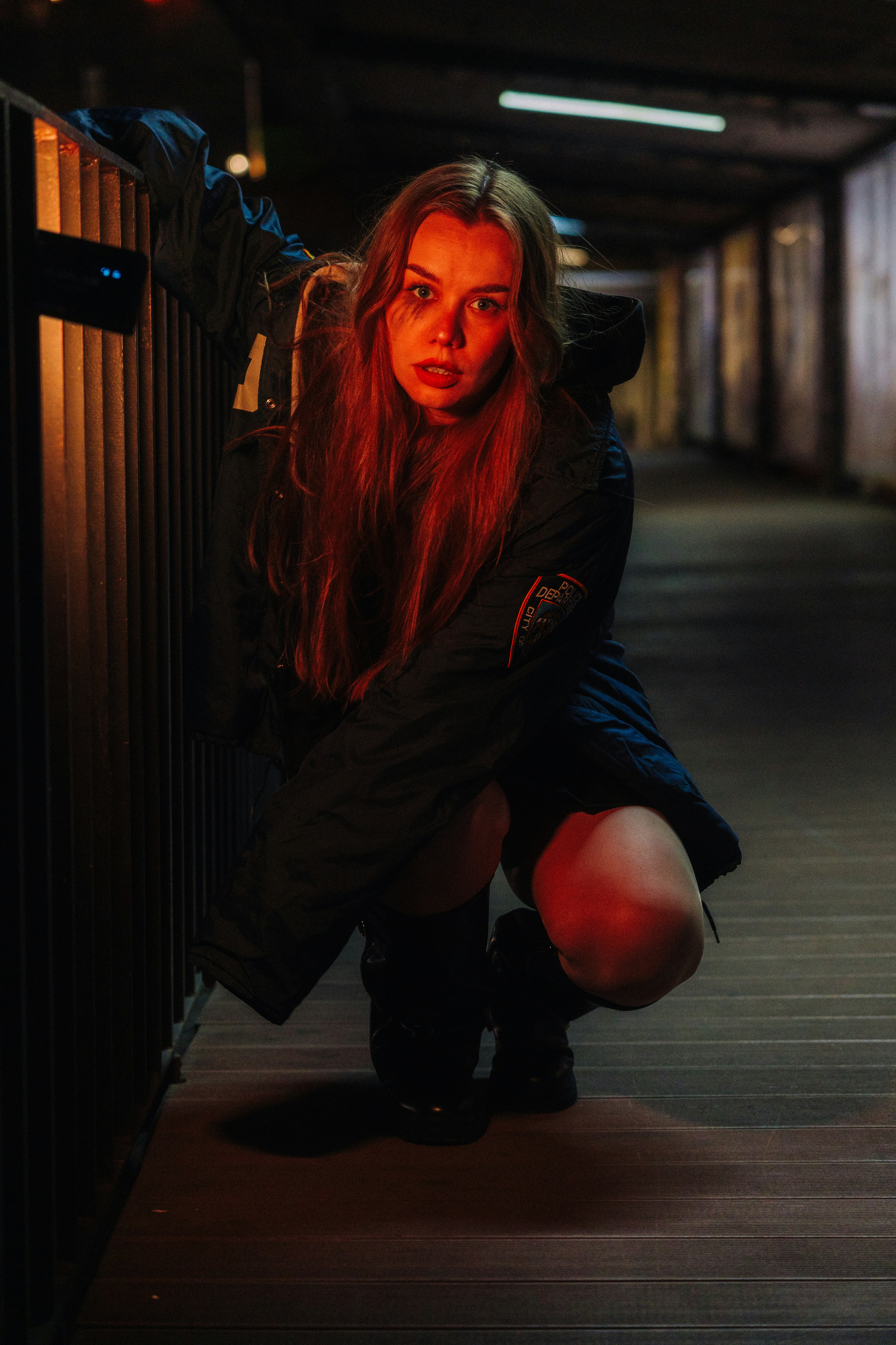 Woman crouching in a dark hallway with red lighting.