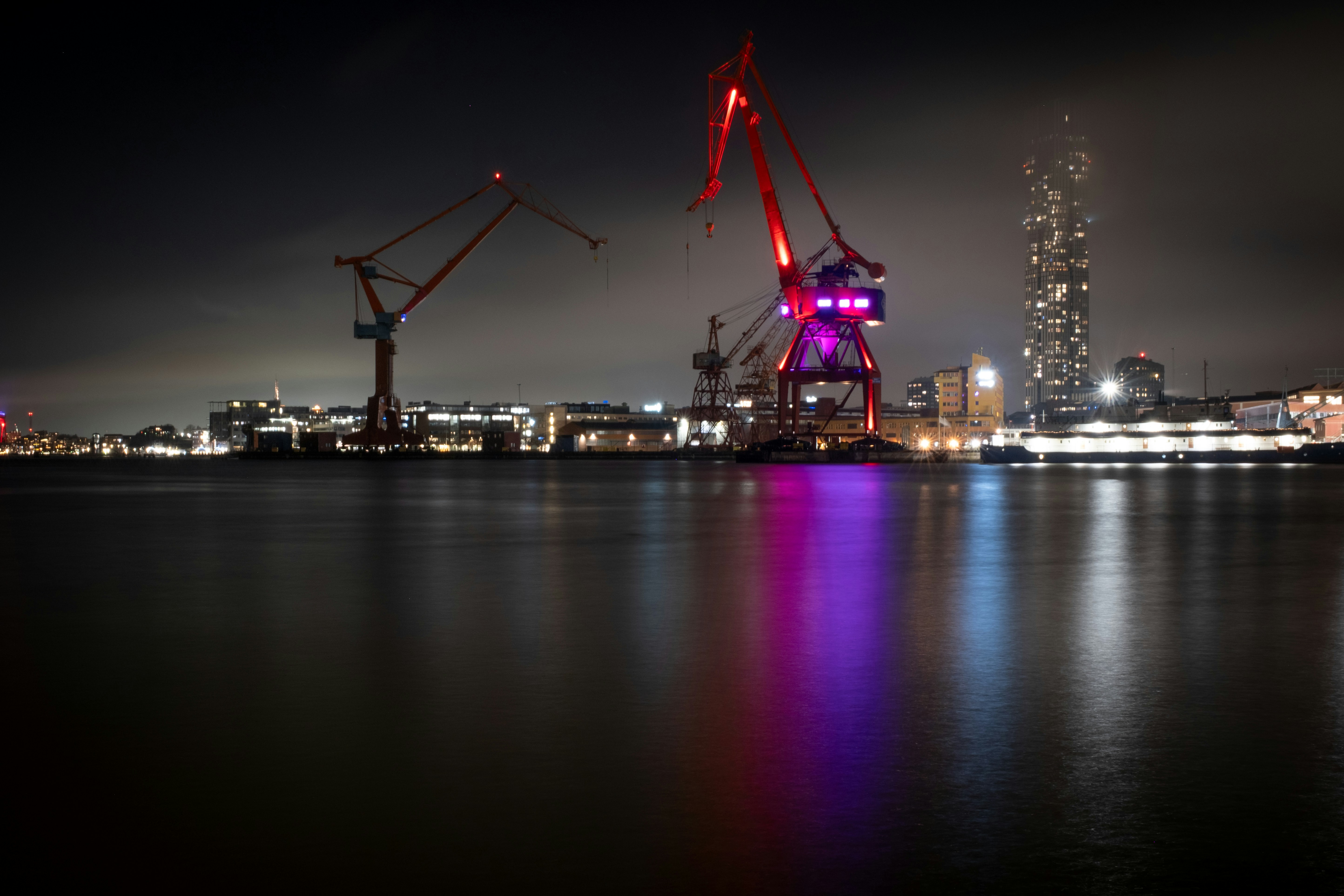 Industrial cranes illuminated at night by a harbor.