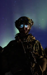 Soldier with glowing eyes under the aurora borealis.
