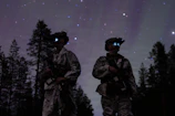 Two soldiers with night vision goggles under starry sky