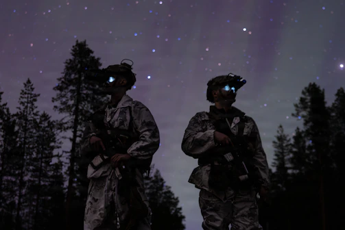 Two soldiers with night vision goggles under starry sky