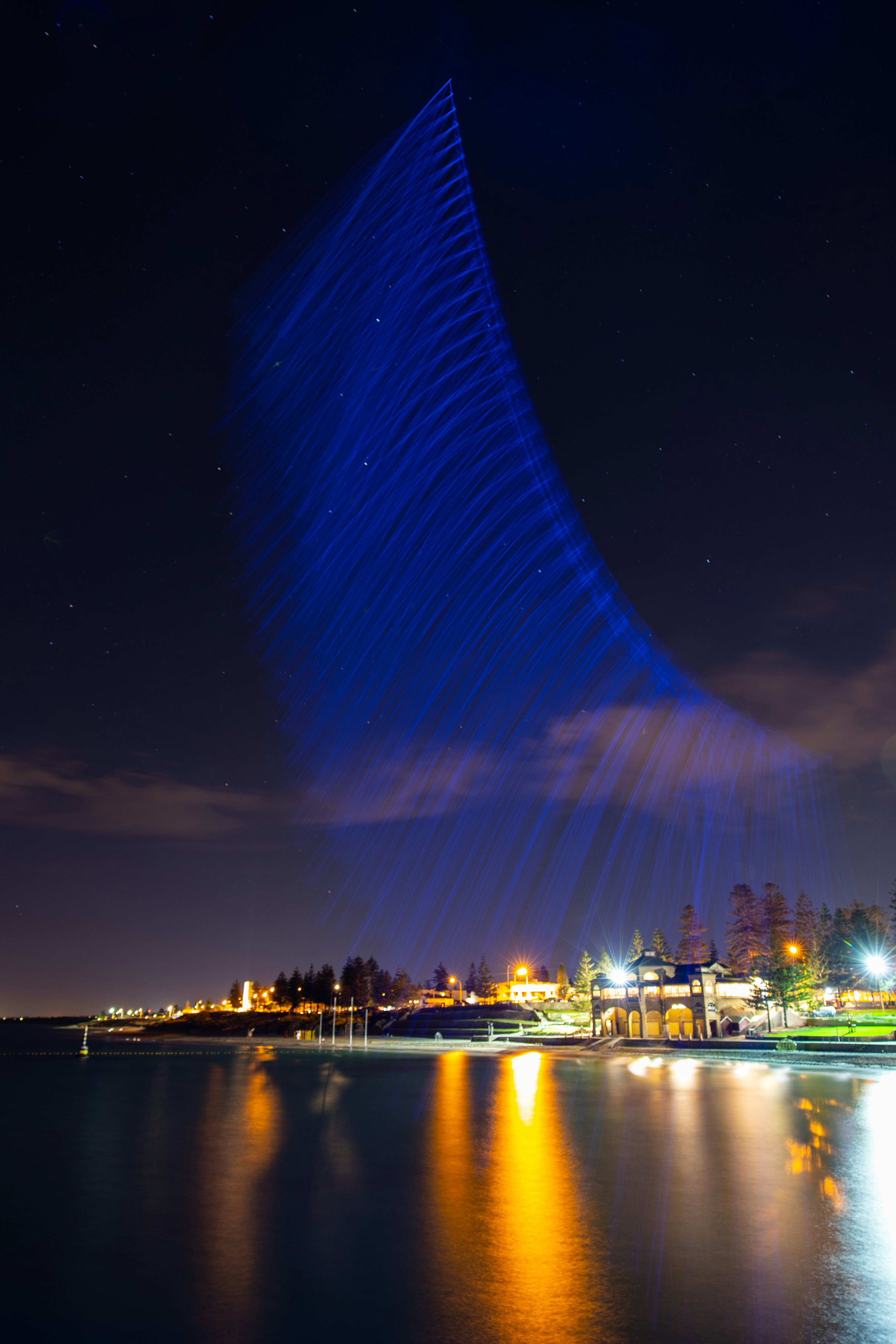 Blue light streaks across night sky over water