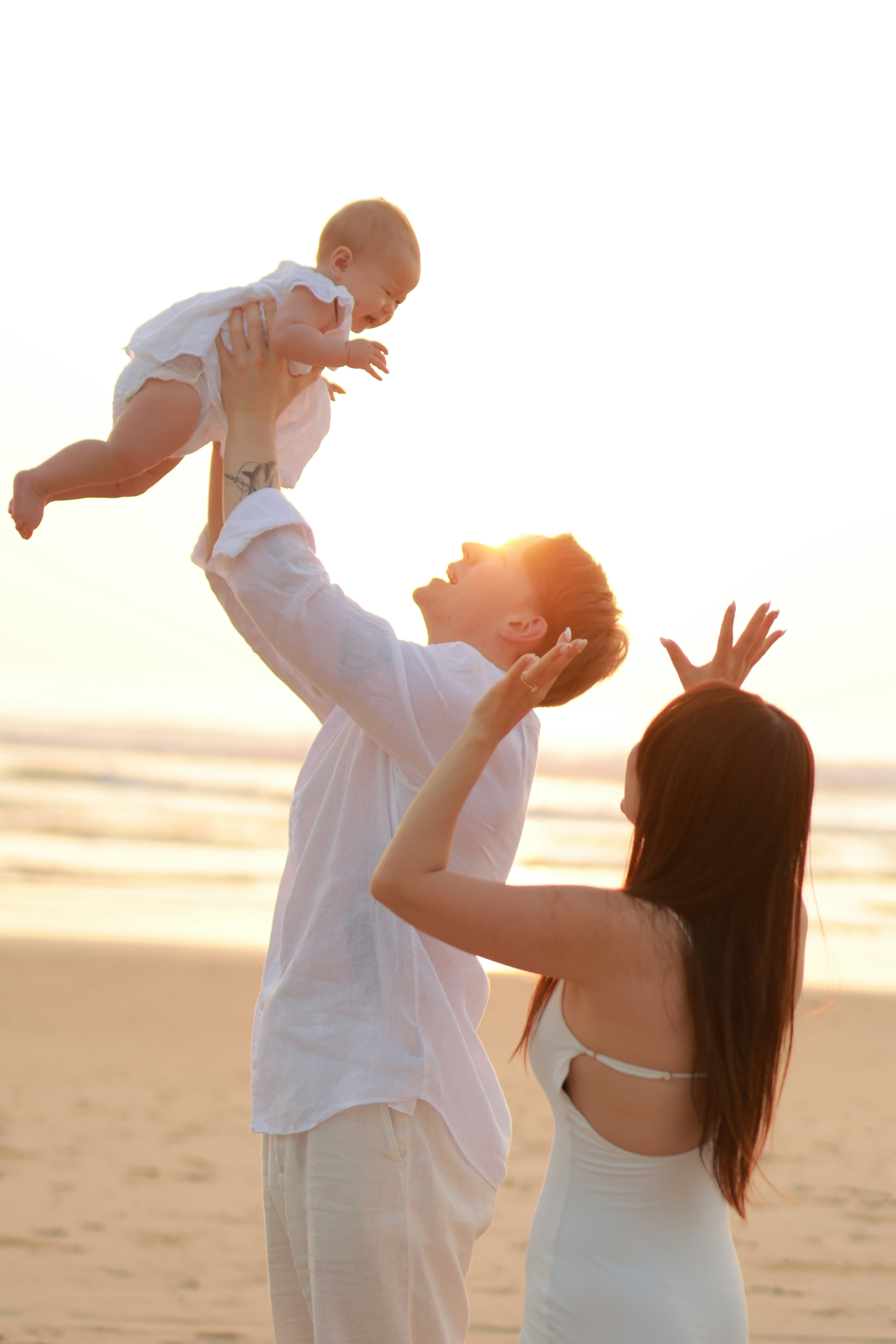 Family playing with baby on beach at sunset
