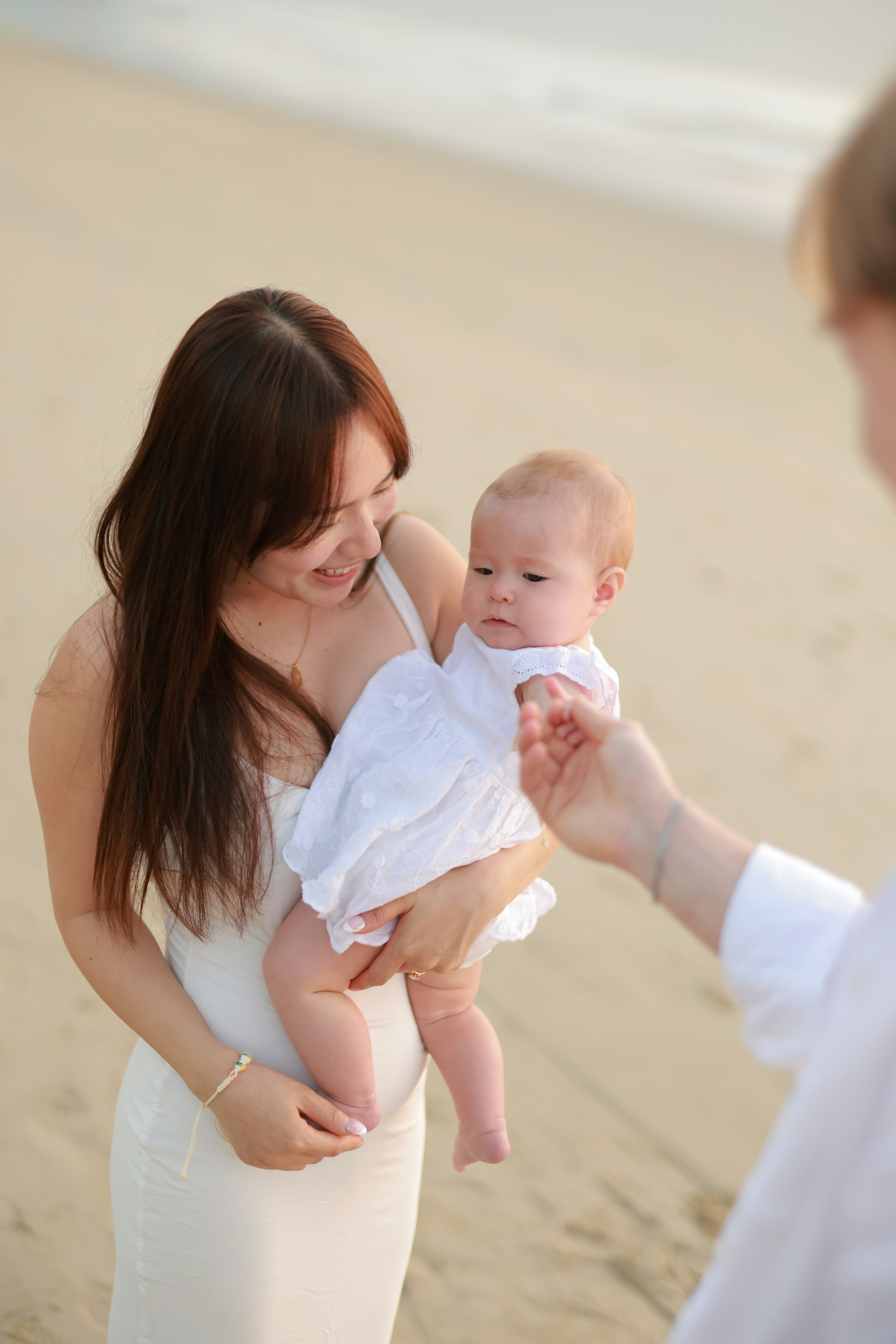 Mother holding baby on a sandy beach.