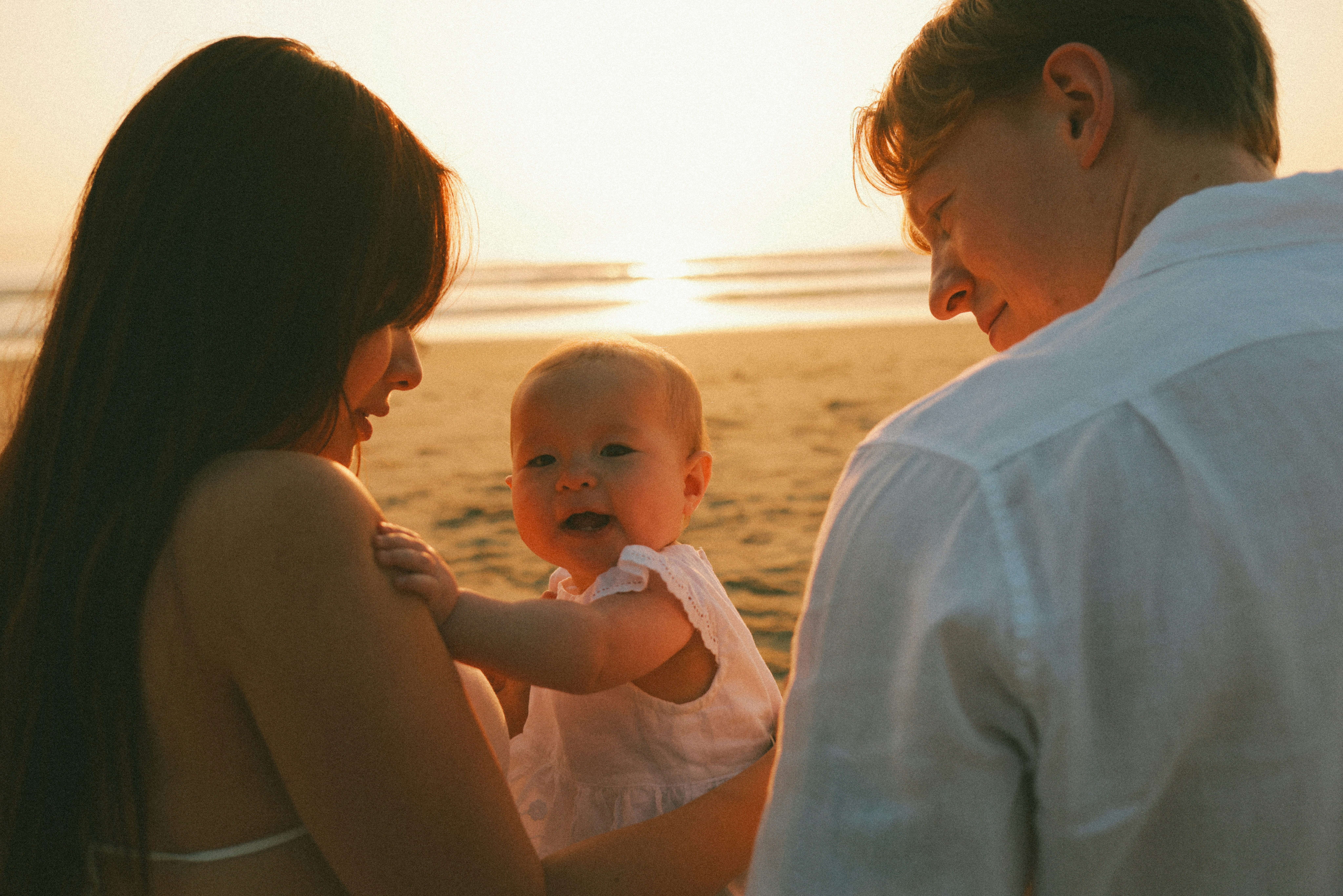 Parents holding baby on a beach at sunset