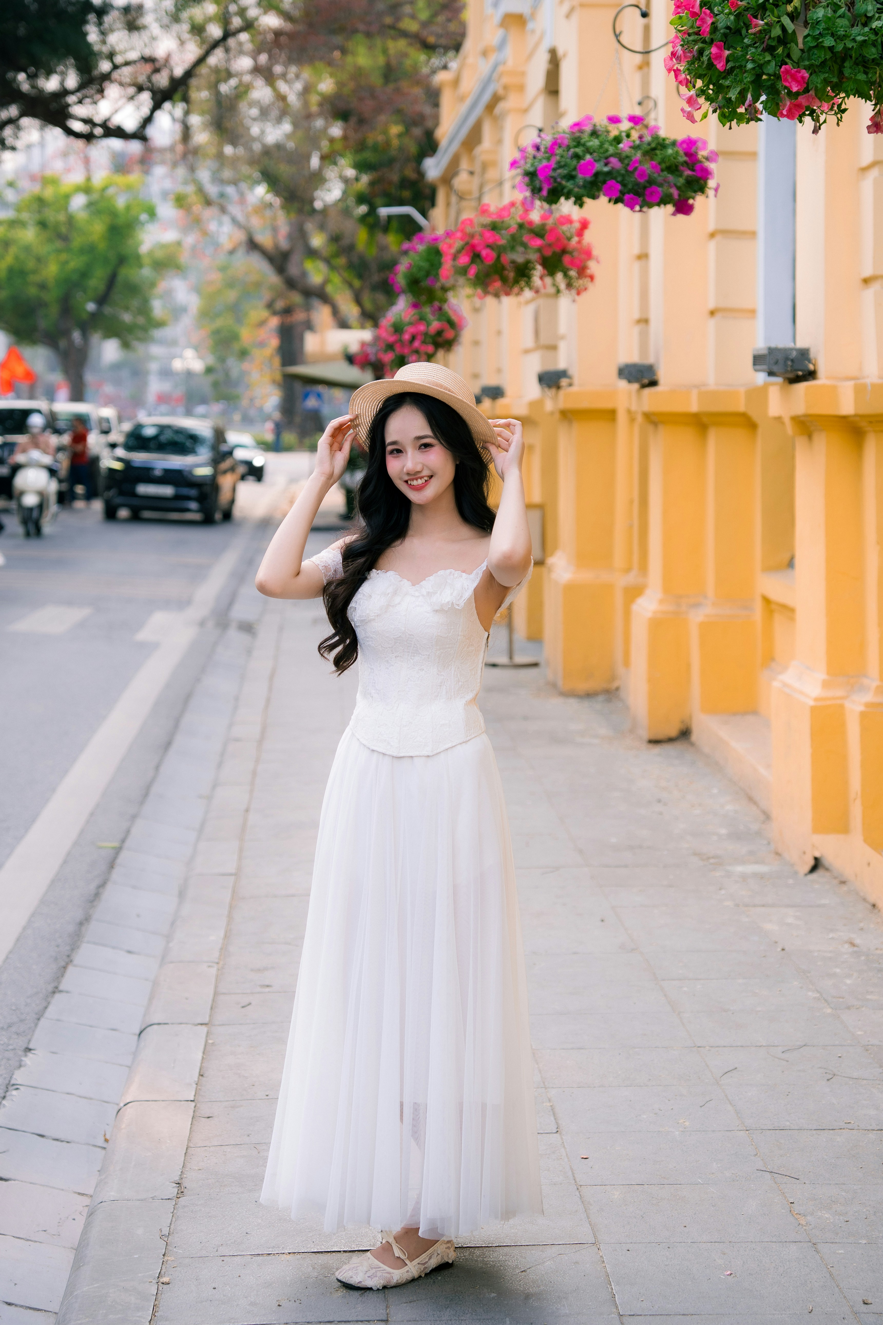 A serene portrait of a young woman in a white dress by the lakeside, surrounded by blooming flowers in Hanoi.