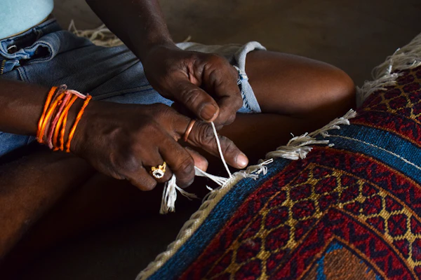 Artisan hands tying fringe on a vibrant woven rug — community craft skills and cultural heritage