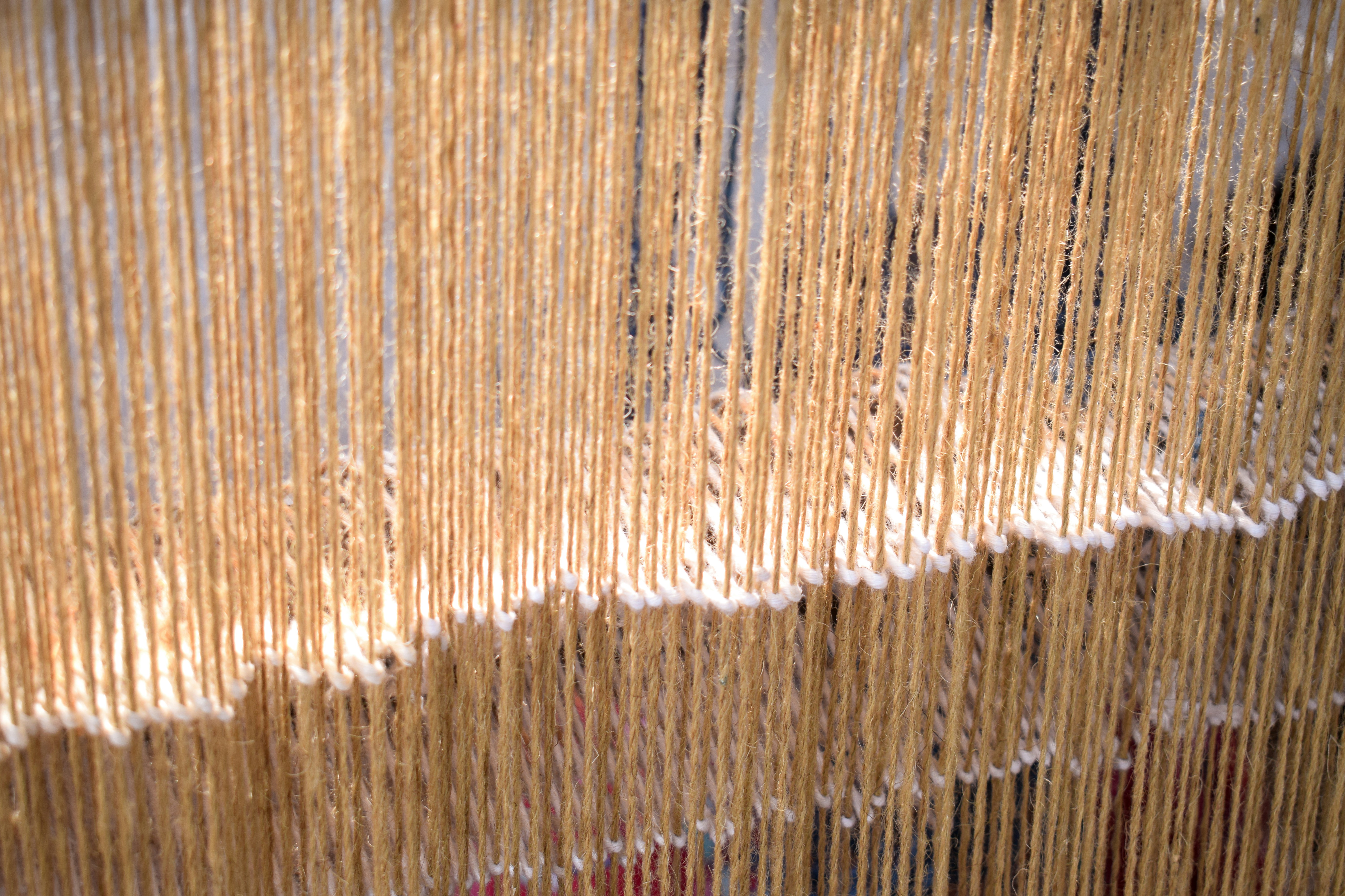 Close-up of hanging golden threads on a loom.