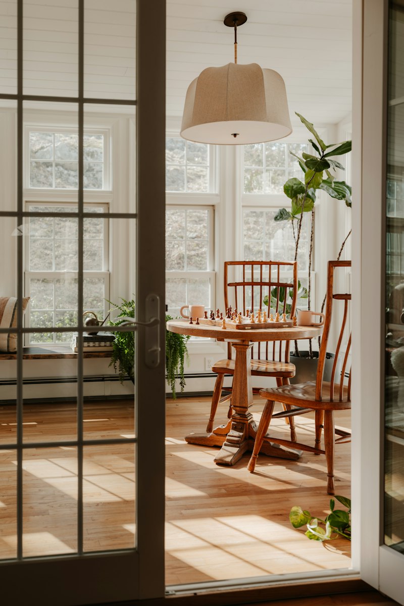 Sillas de comedor de madera clara alrededor de una mesa junto a una ventana con luz natural