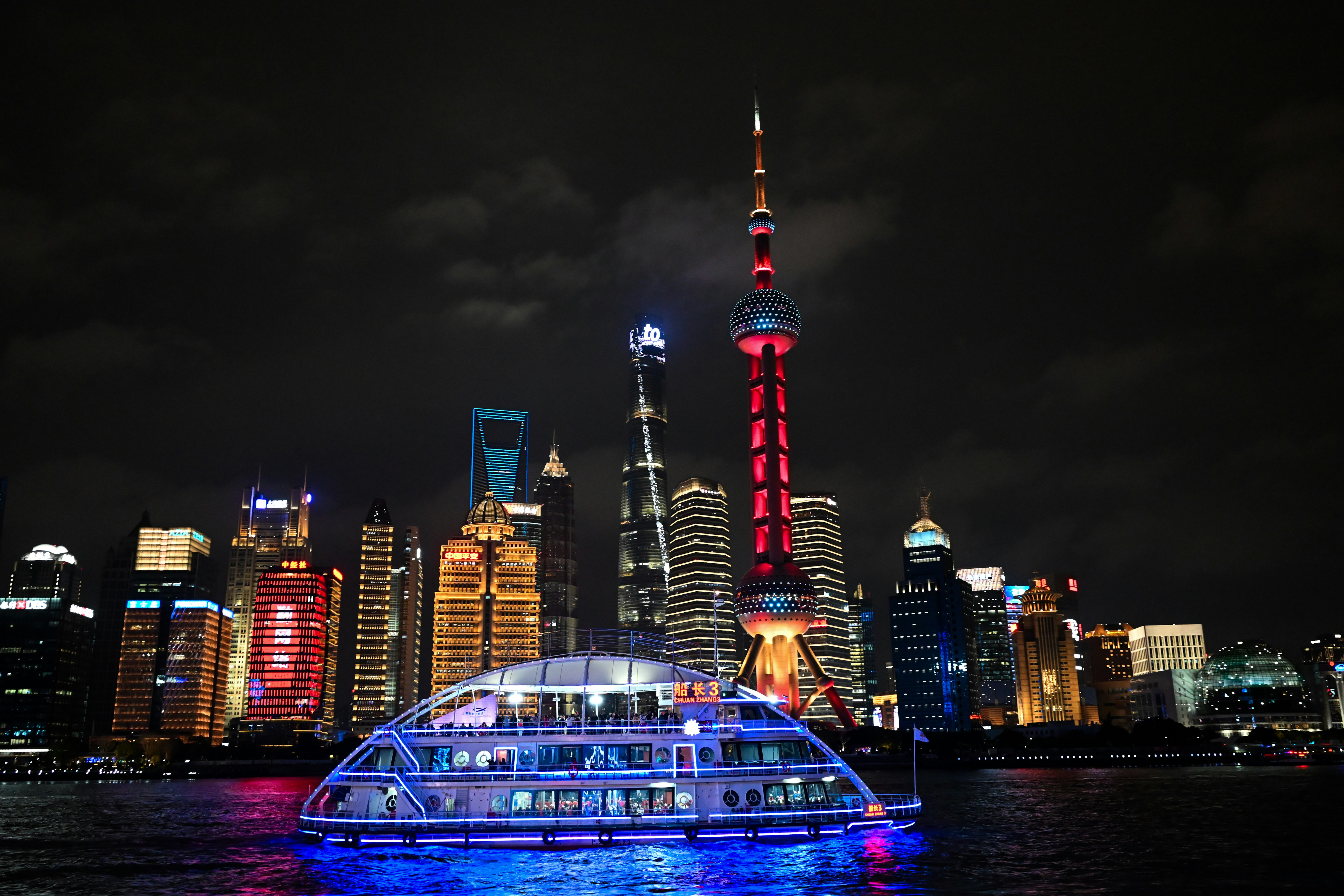 Un bateau lumineux navigue sur l’eau la nuit.