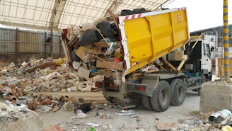 A yellow truck dumping trash at a facility