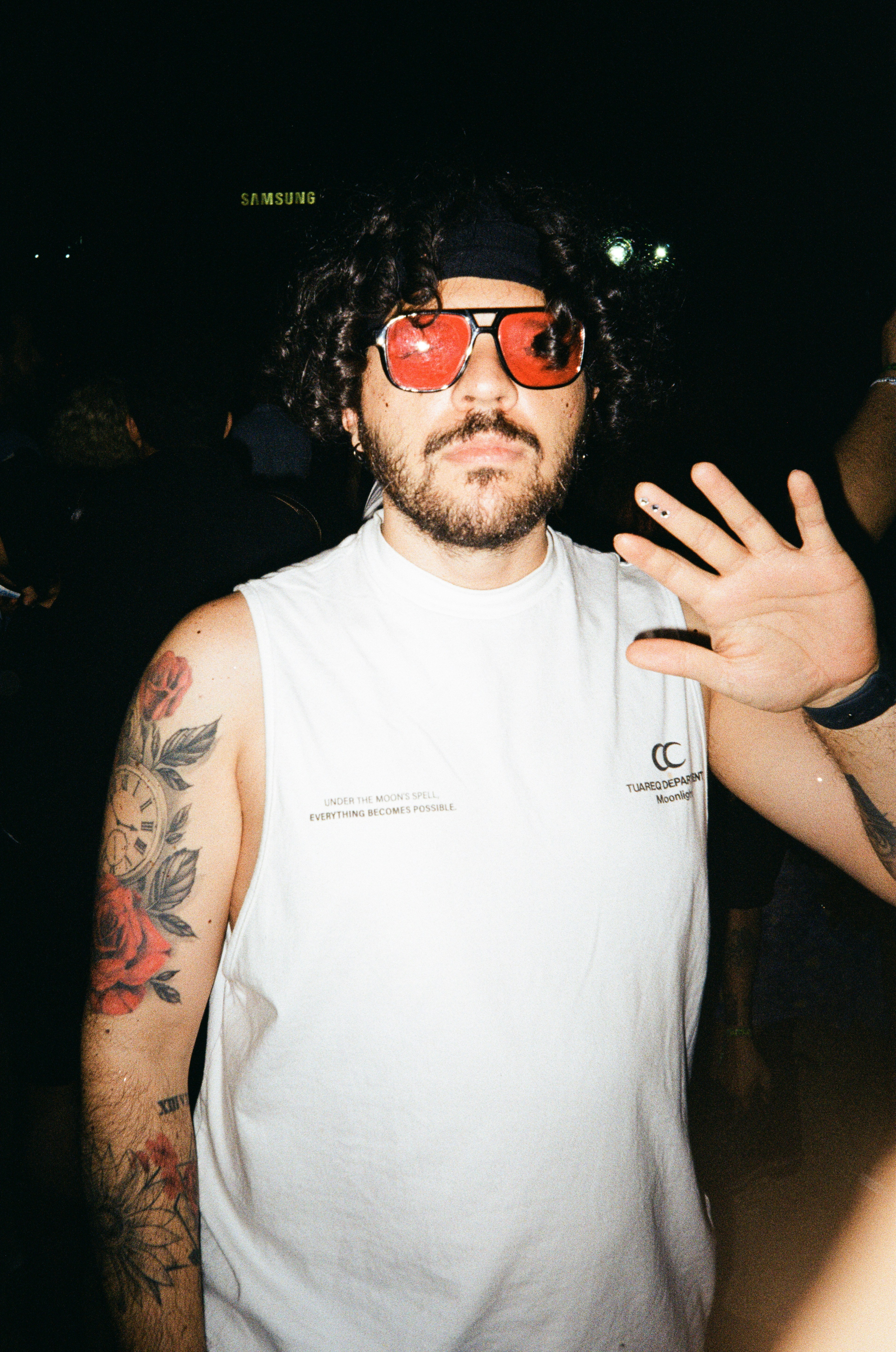 Man with bandana and red sunglasses waves hand