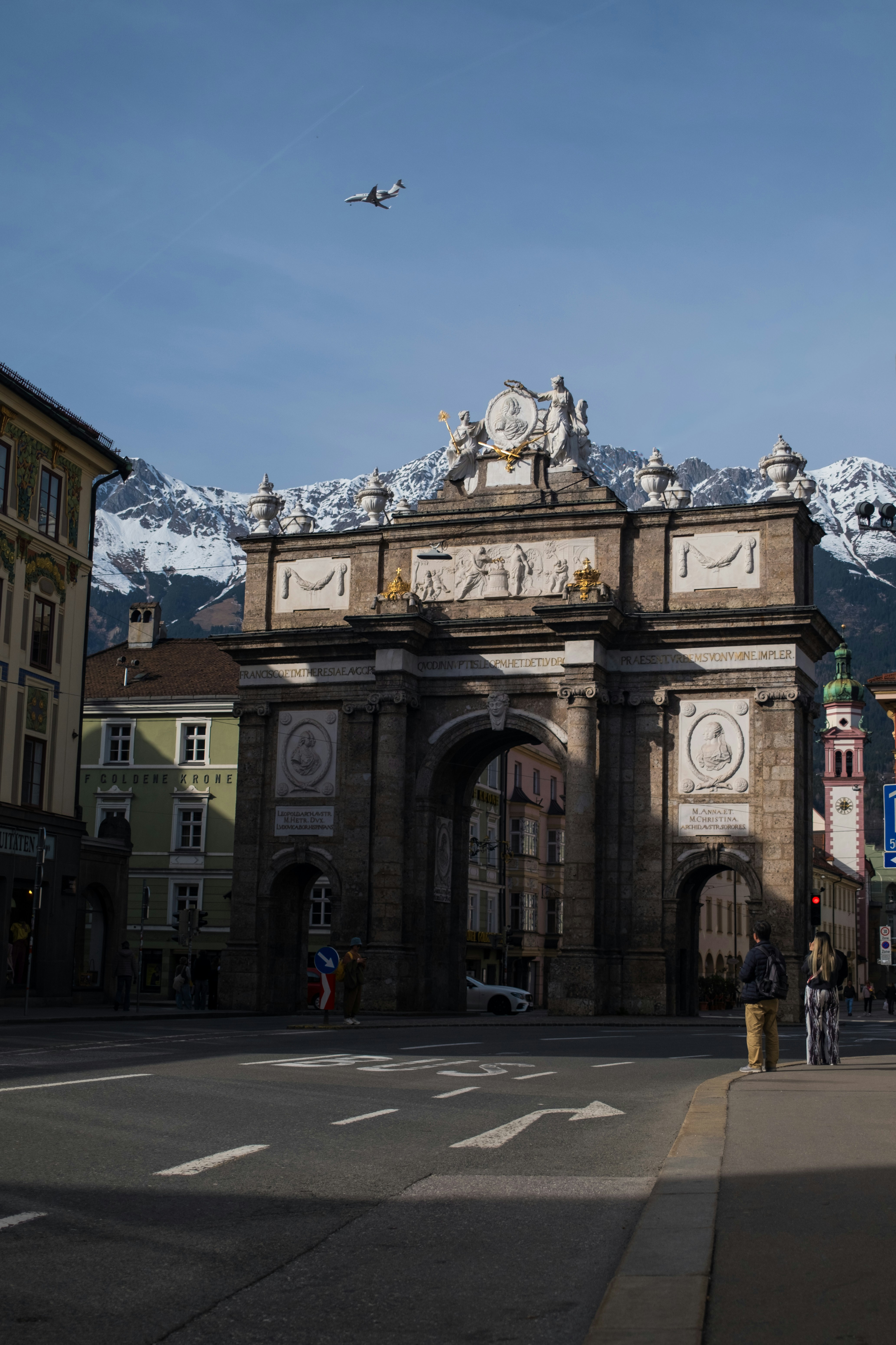 Triumphal arch with snow-capped mountains and airplane.