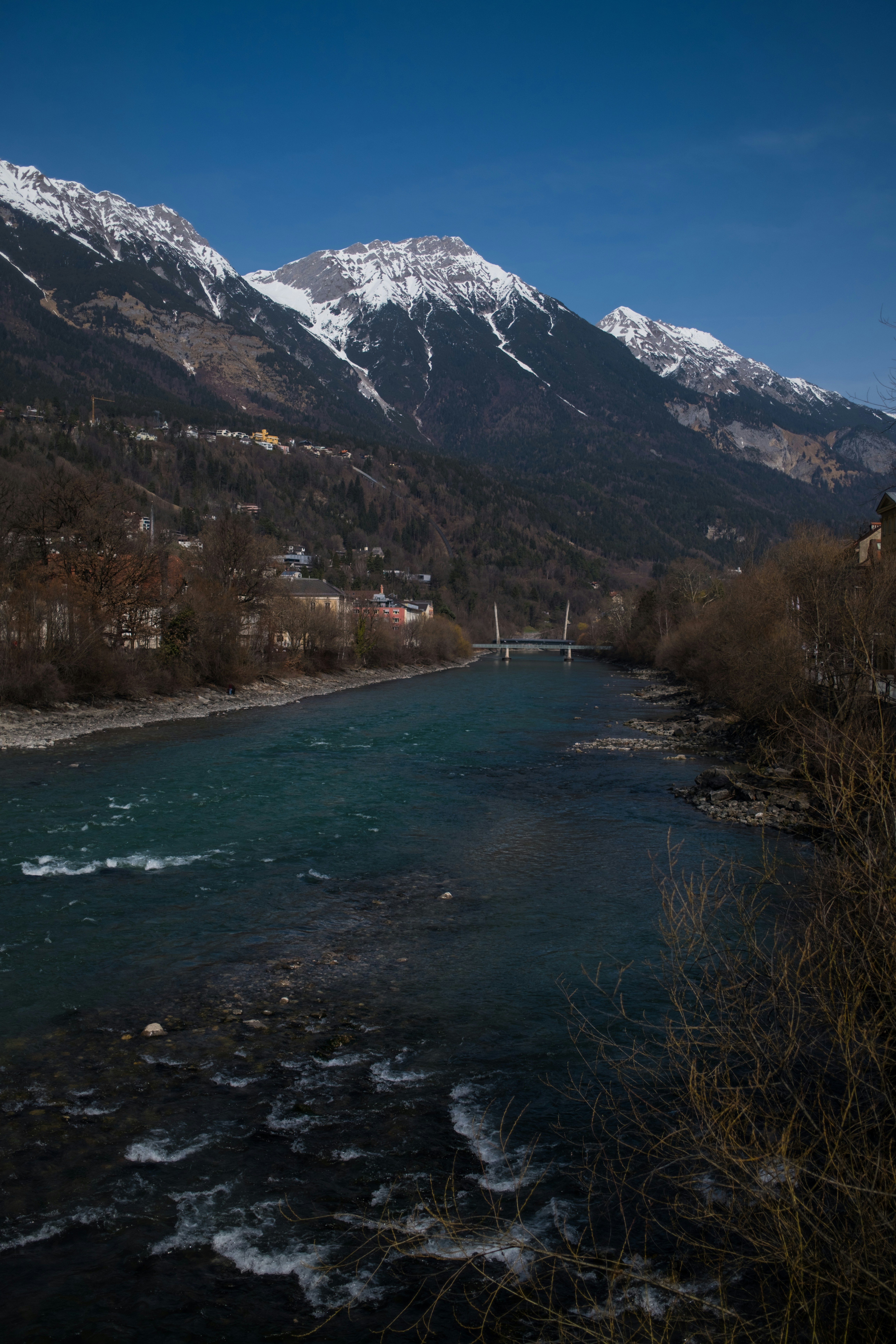 A wide river flows through a valley with snowy mountains.