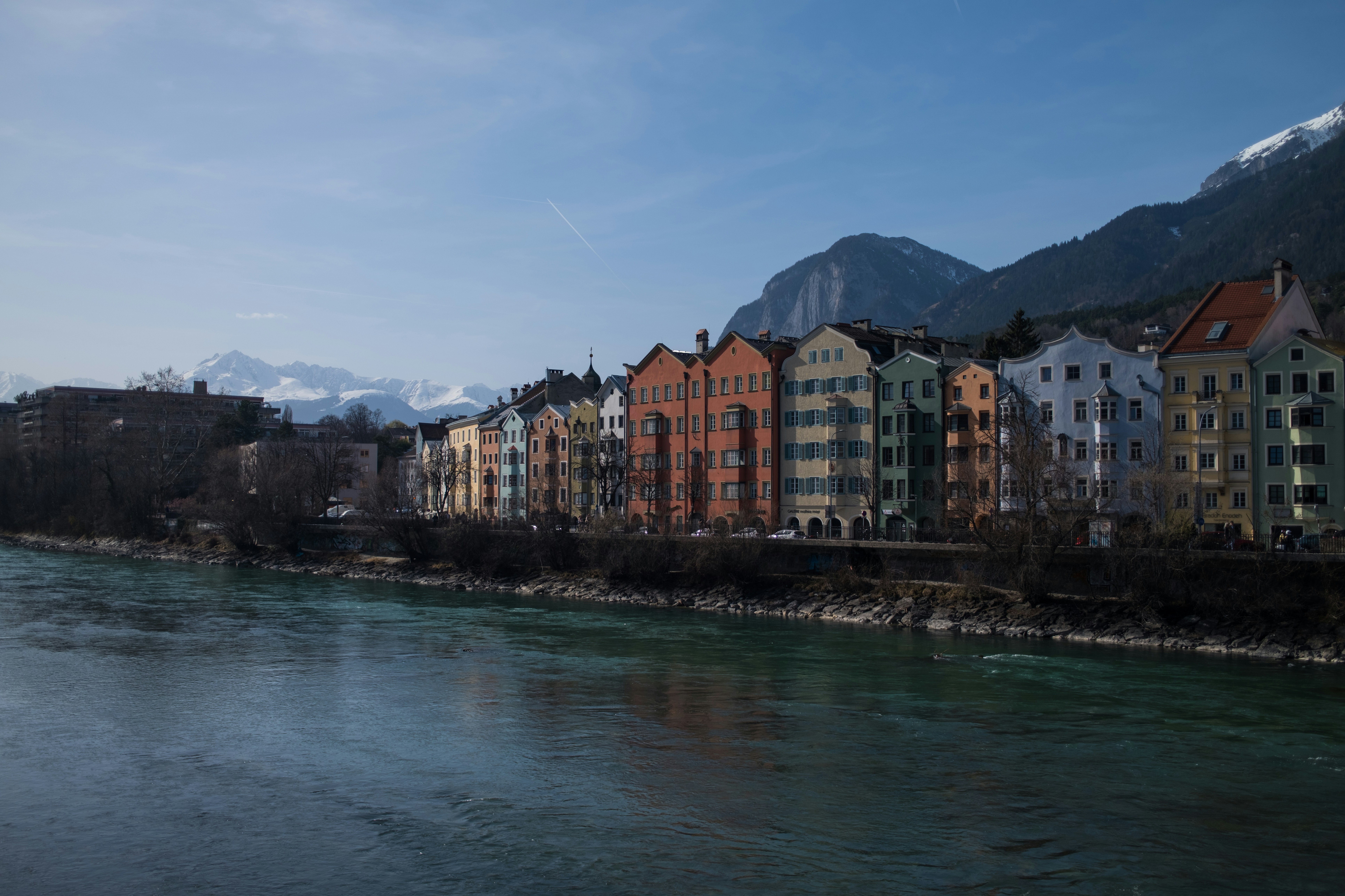 Colorful buildings line a river with mountains behind.