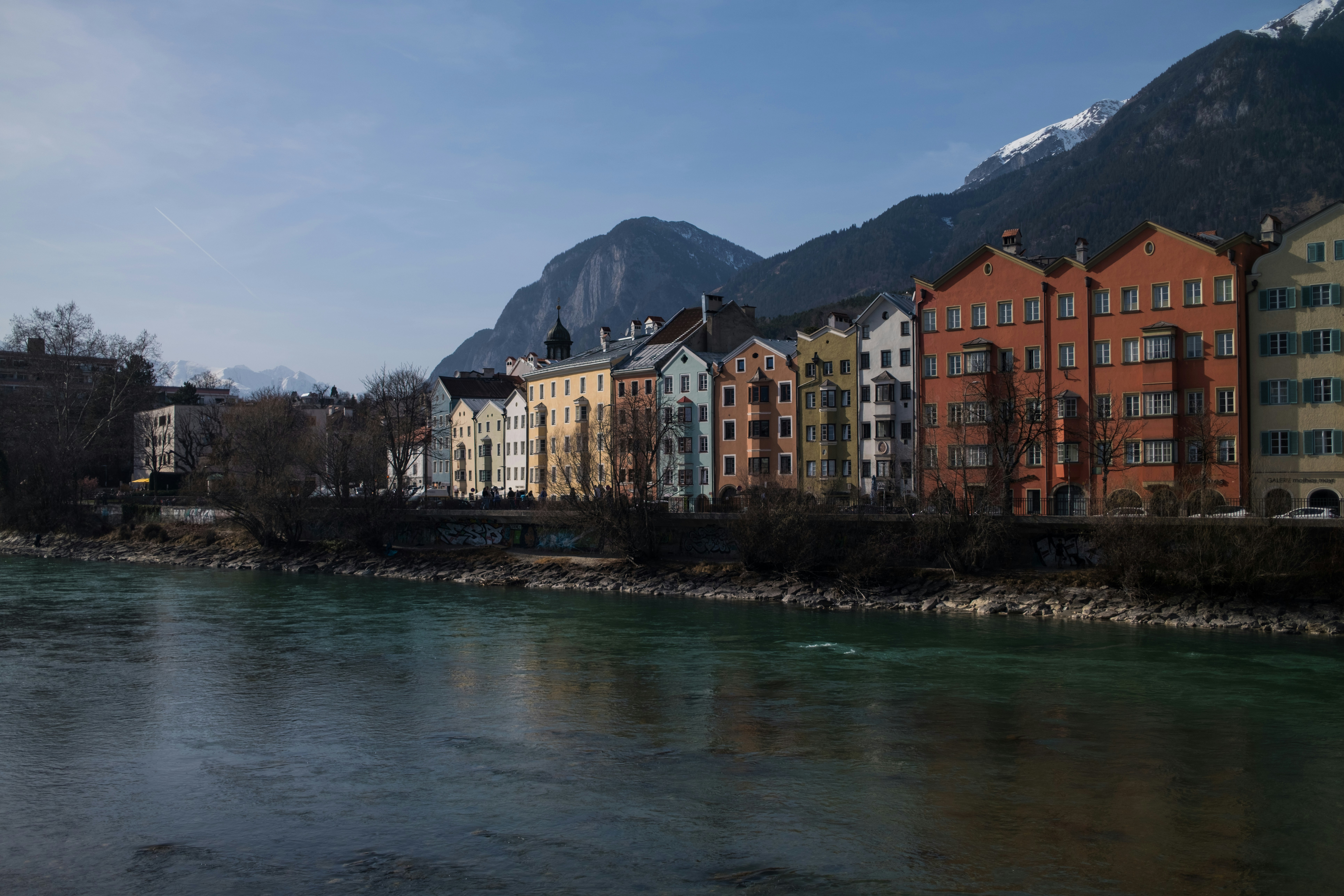 Colorful buildings line a river with mountains behind.