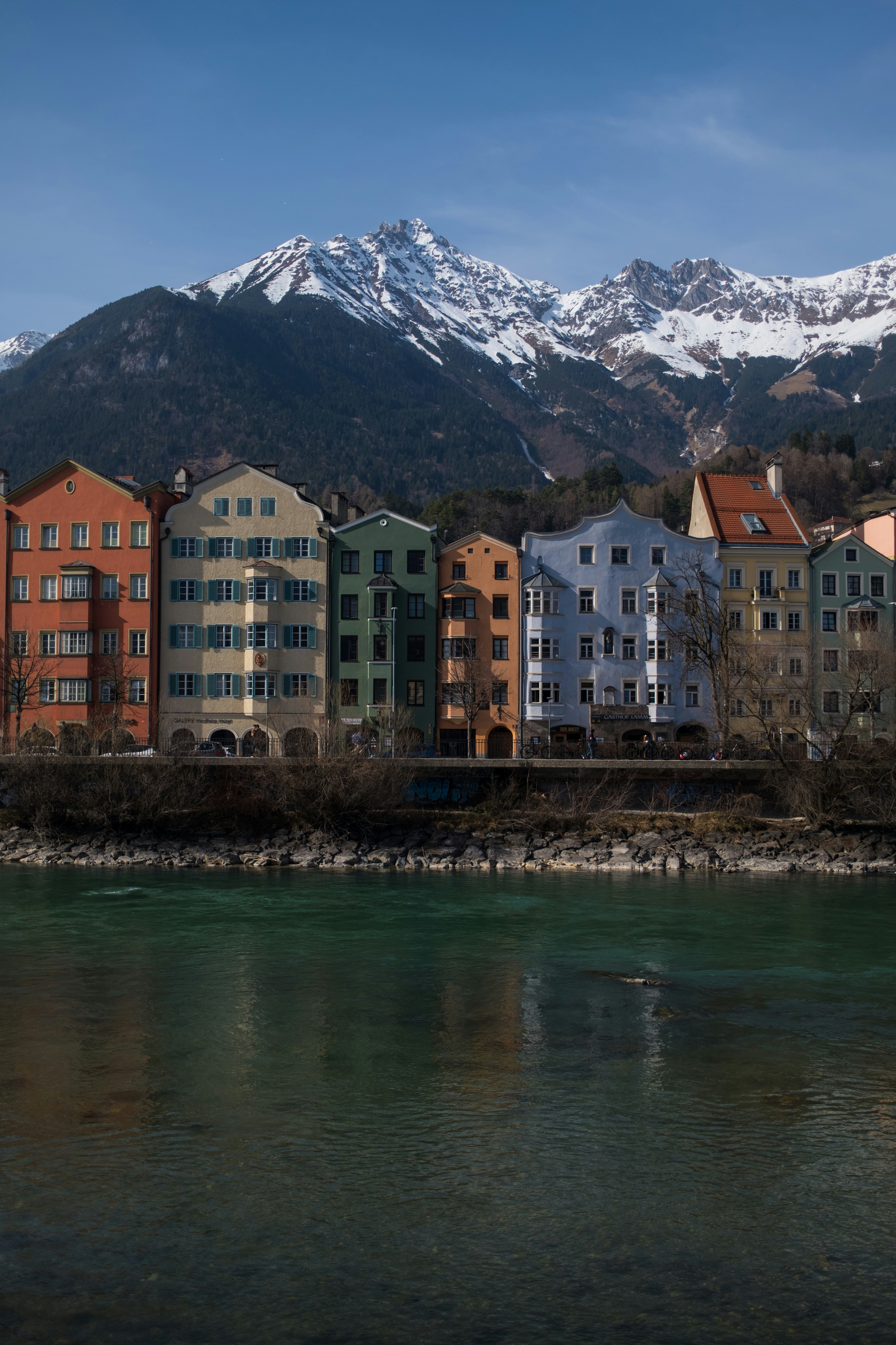 Colorful buildings line a river with snowy mountains behind.