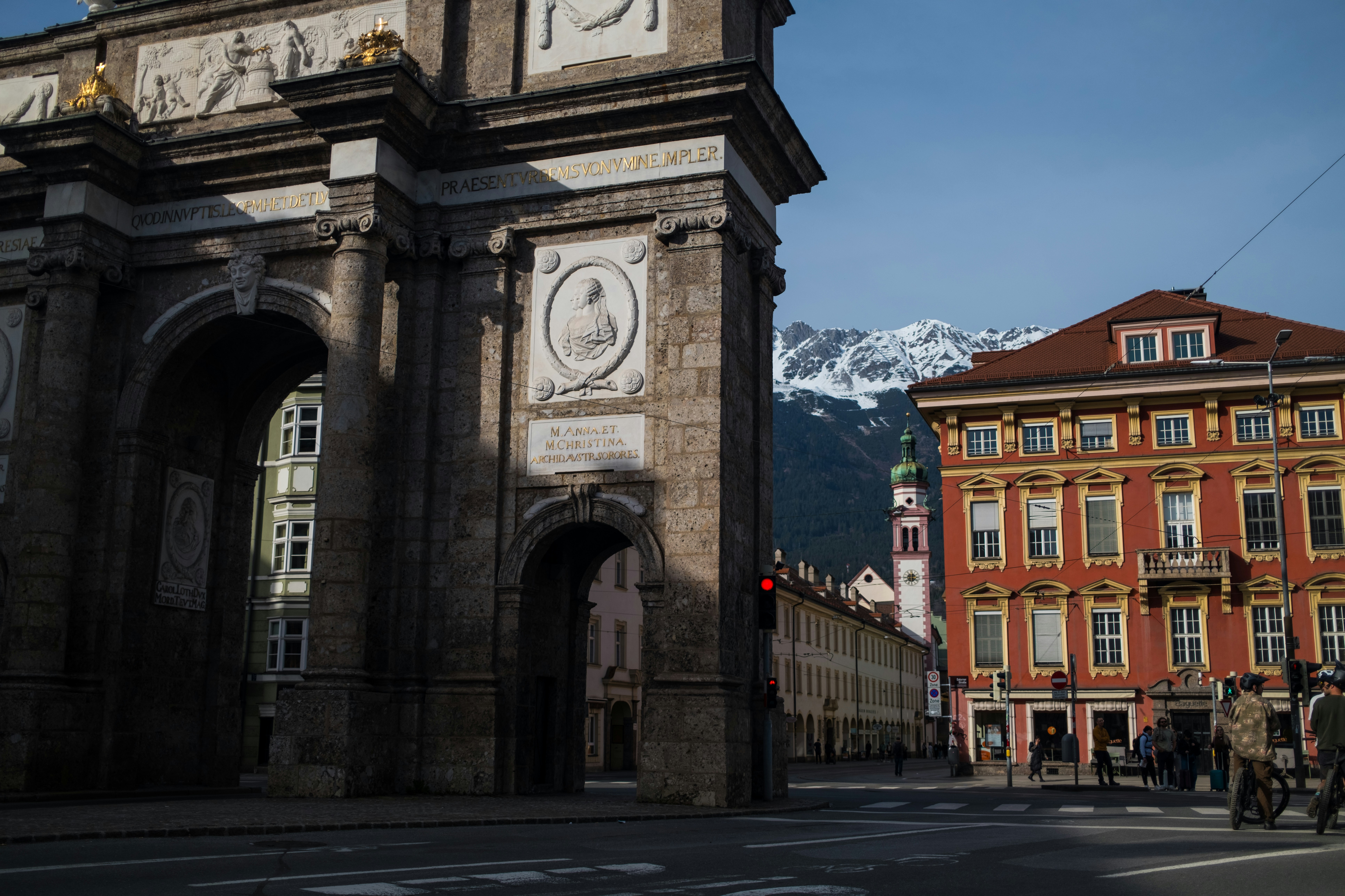 Triumphal arch with colorful buildings and snowy mountains.