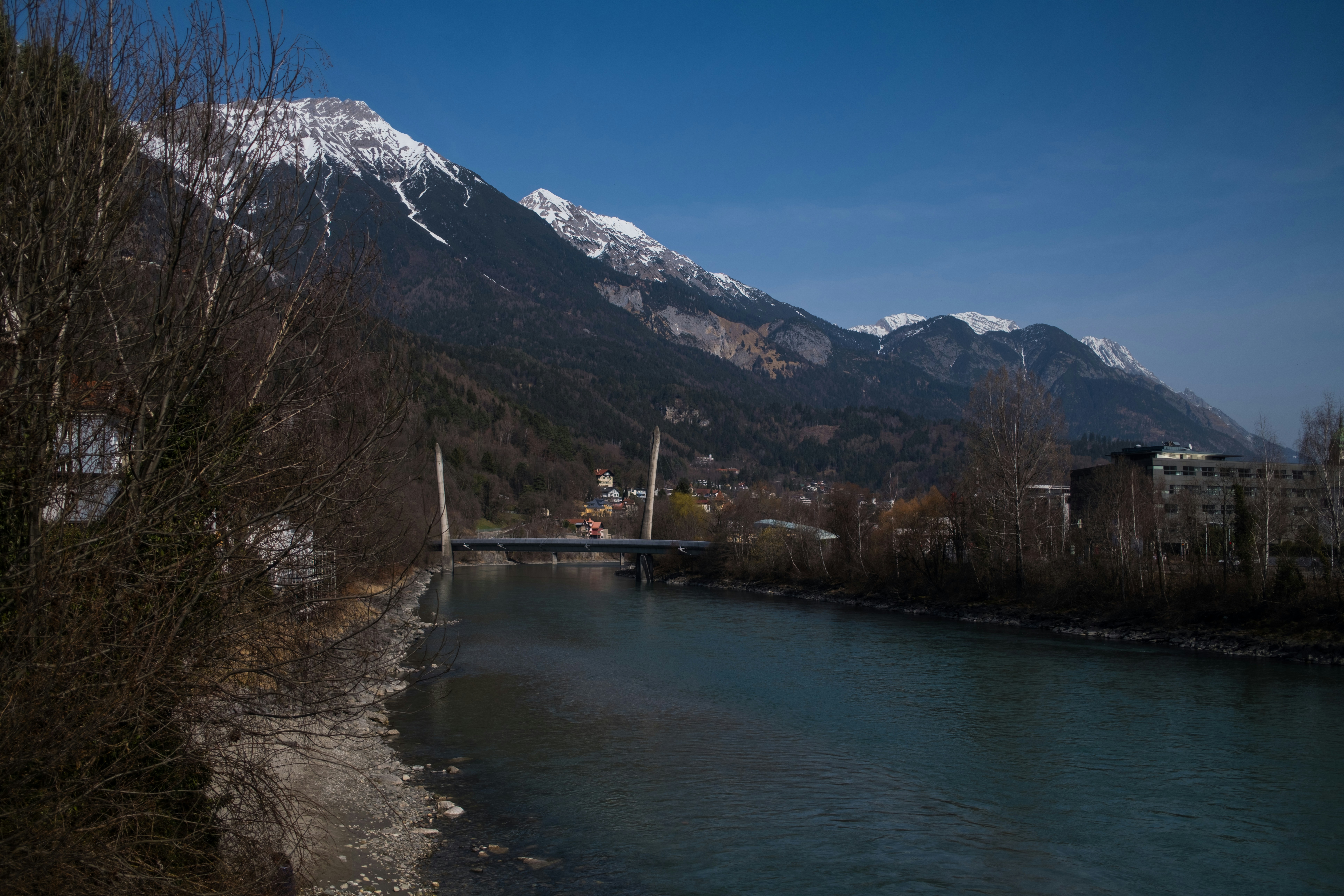 A bridge crosses a wide river with snowy mountains behind.