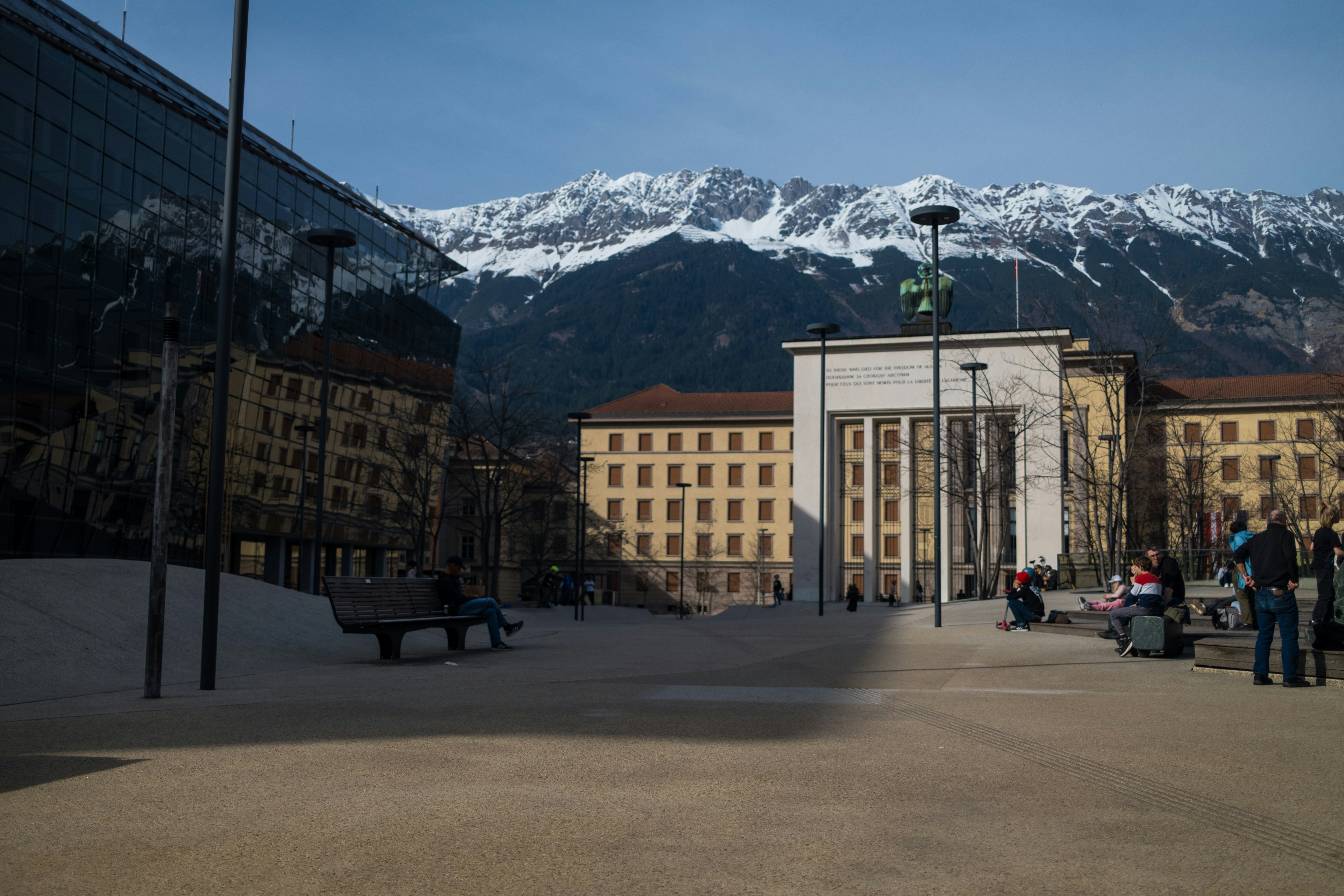 Modern building reflects snowy mountains in a plaza.
